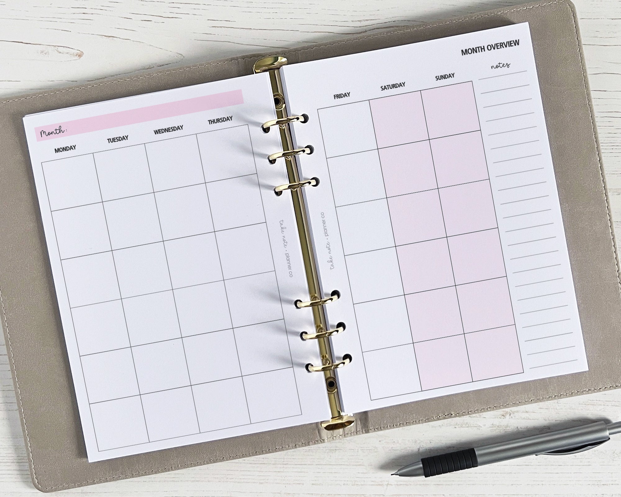 An open monthly planner insert with a classic design, featuring a two-page spread with good sized boxes and a side panel for additional notes, lying flat on a surface with a pen beside it.