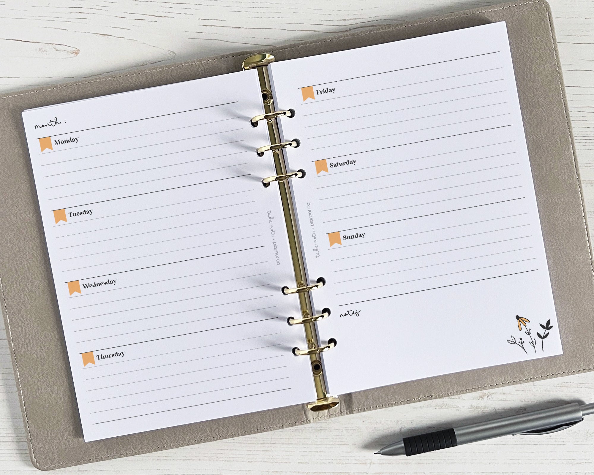 A floral undated weekly planner insert in a ringbinder with a pen on a white wooden background.