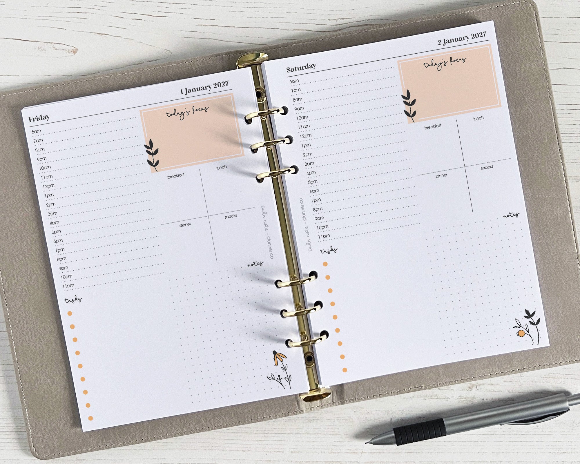 A5 daily planner inserts with a floral design, featuring a day-to-page layout with time slots, a to-do list, and notes section, lying flat on a surface with a pen alongside.