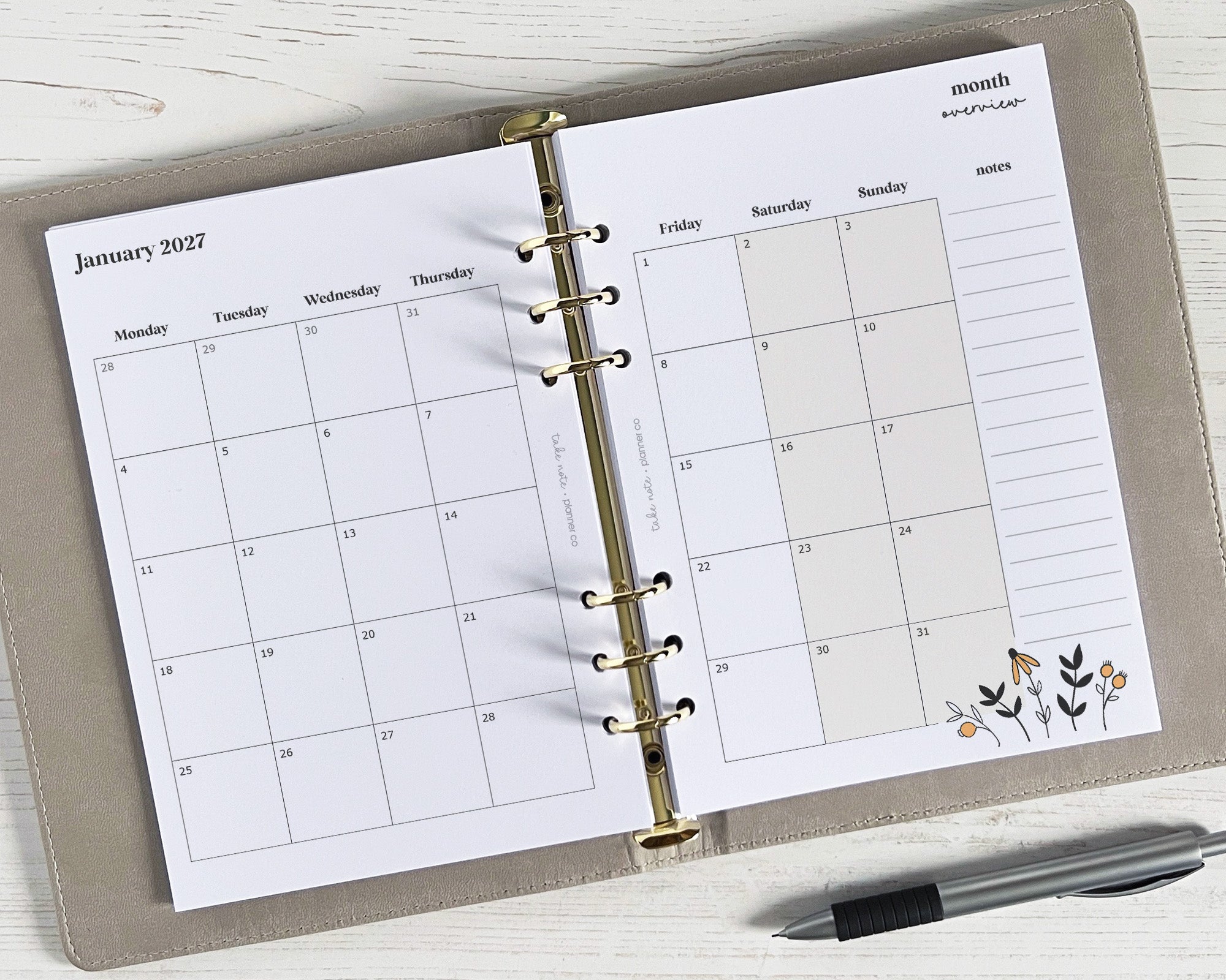 A5 monthly planner inserts with a floral design, displayed in a binder with a pen for scale.