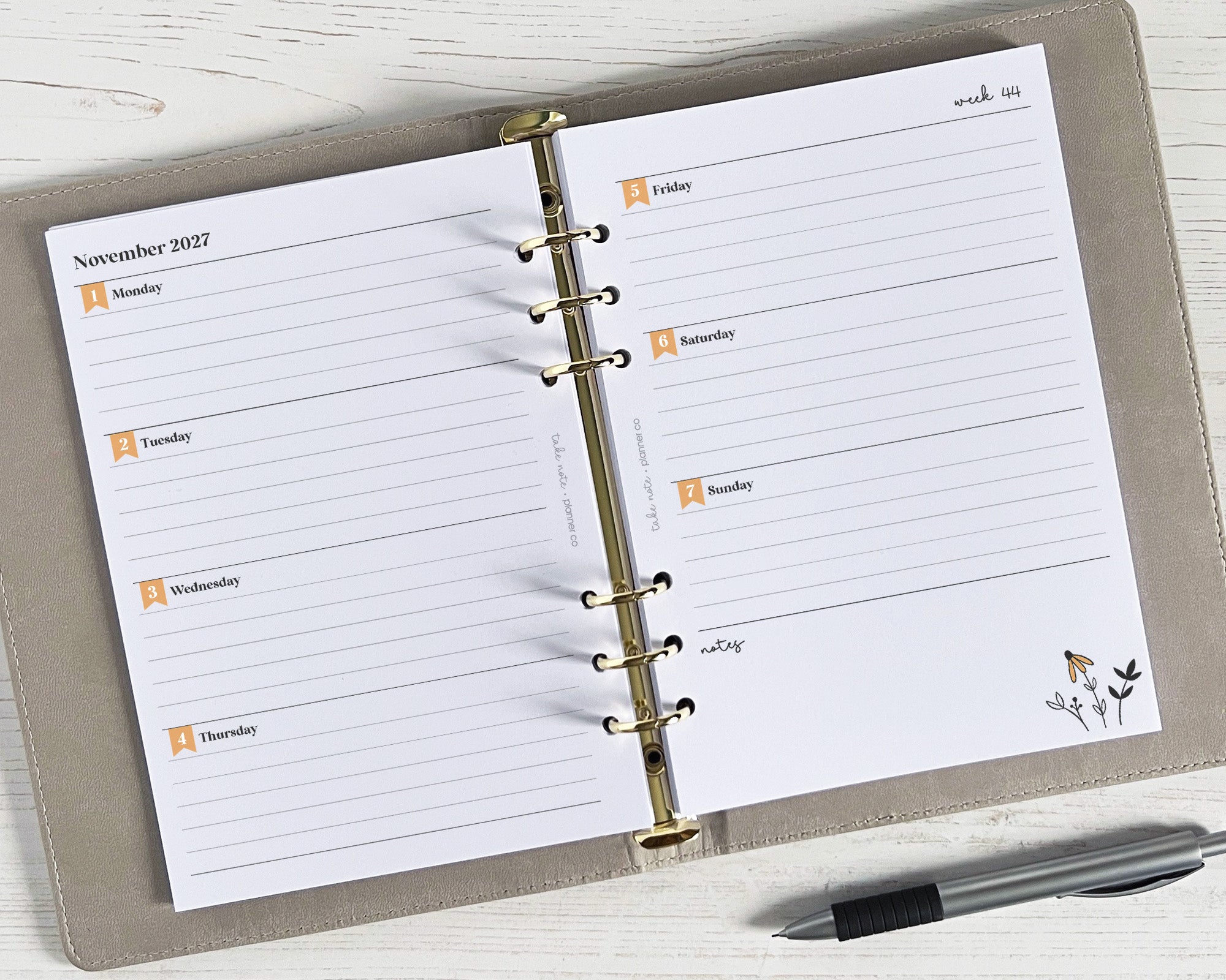 Weekly planner inserts with a floral design, displayed in a binder with a pen on the side, indicating a dated two-page spread for a specific week.