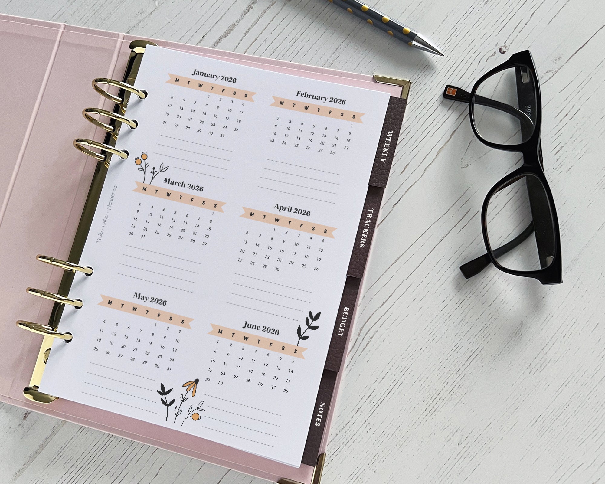 Calendar planner with floral designs on a white surface with glasses and pen