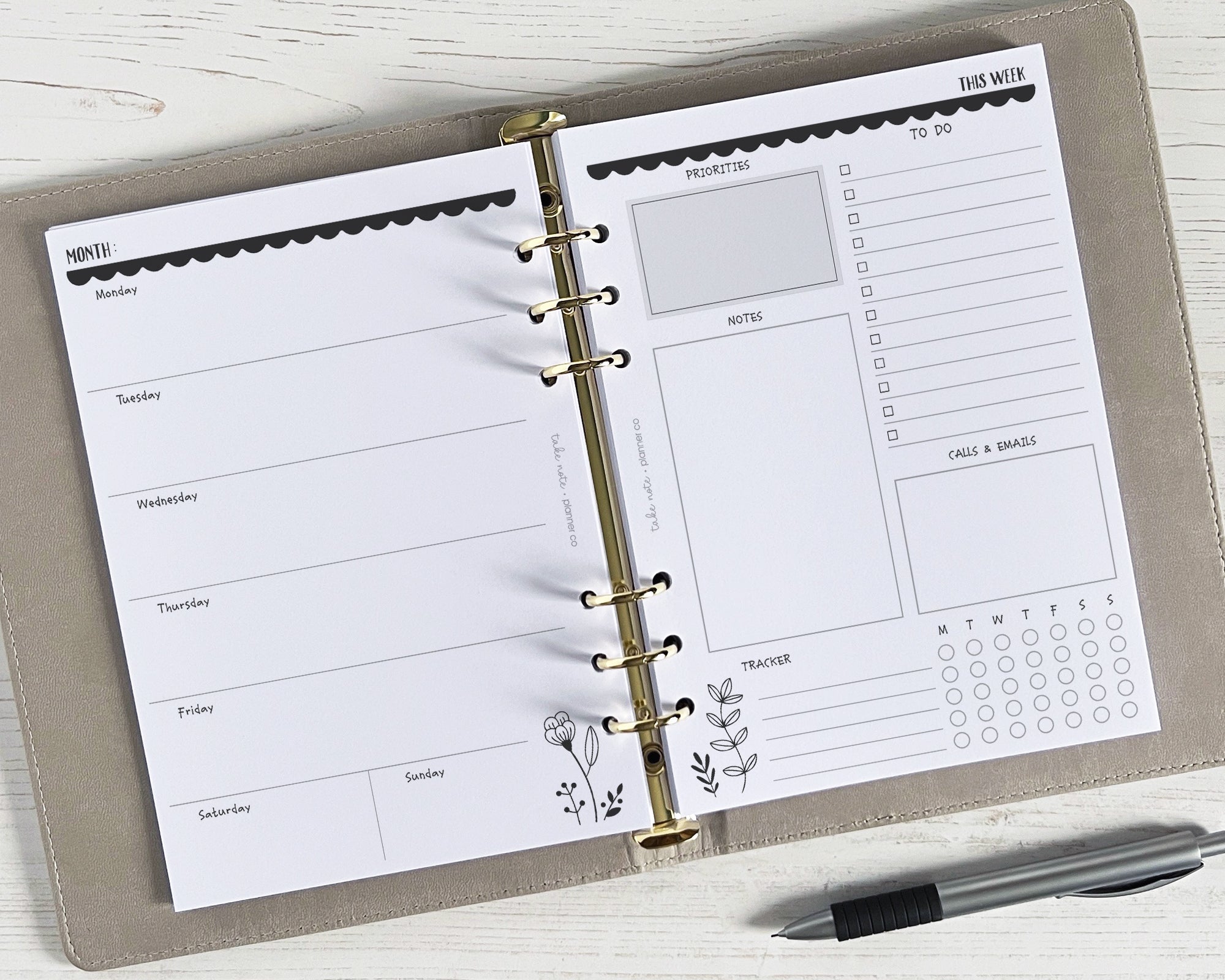 A5 weekly planner inserts with a monochrome floral design, undated, displayed open on a desk with a pen alongside.
