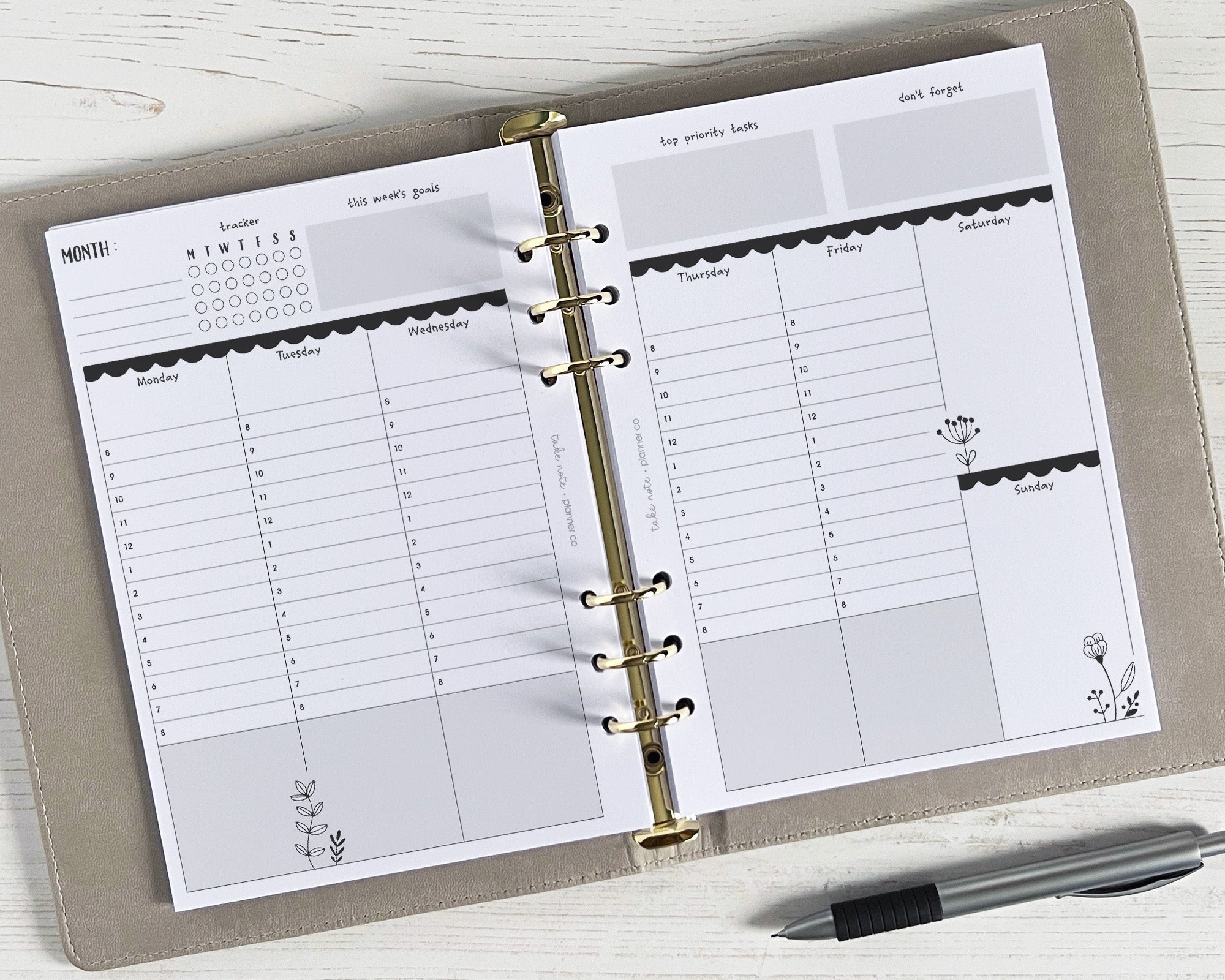 A5 weekly planner inserts with a monochrome floral design, undated, displayed open in a ring binder with a pen lying beside it.