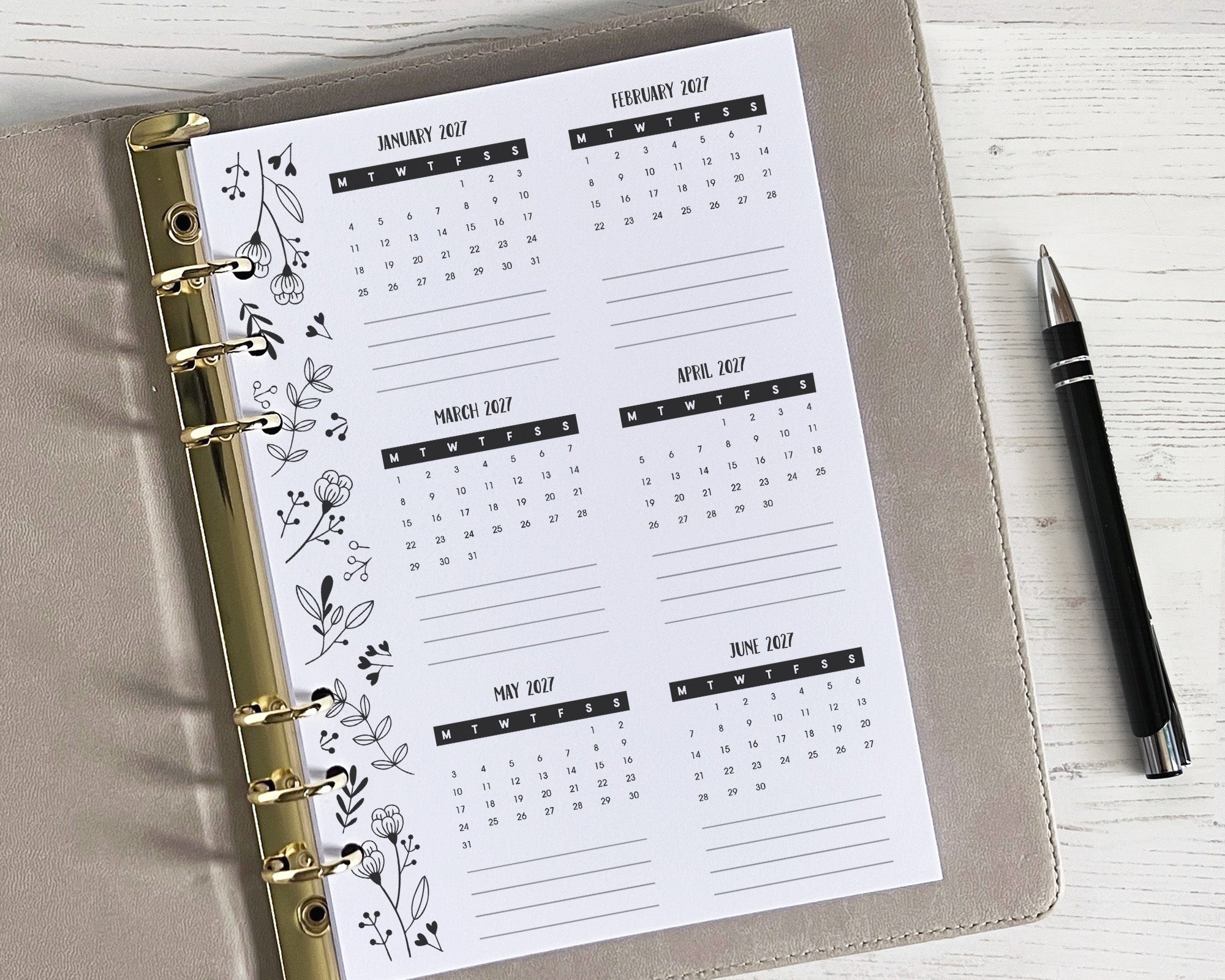 A yearly overview insert with a monochrome floral design, featuring a weekly layout, placed inside a planner binder with a pen beside it.