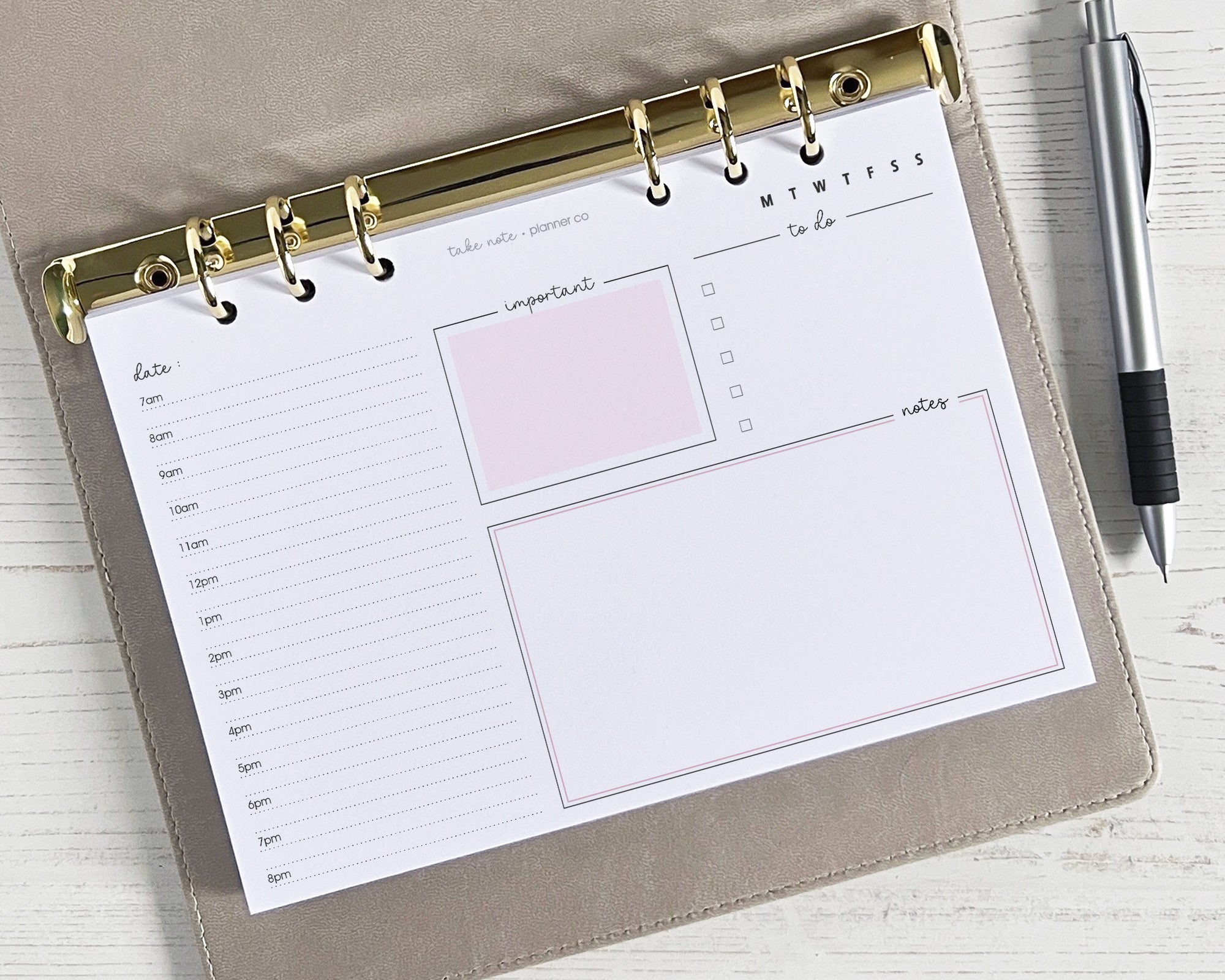 A photo of a daily planner insert with a landscape layout, featuring sections for notes, schedule, priorities, and to-do list, lying on a wooden surface with a pen beside it.