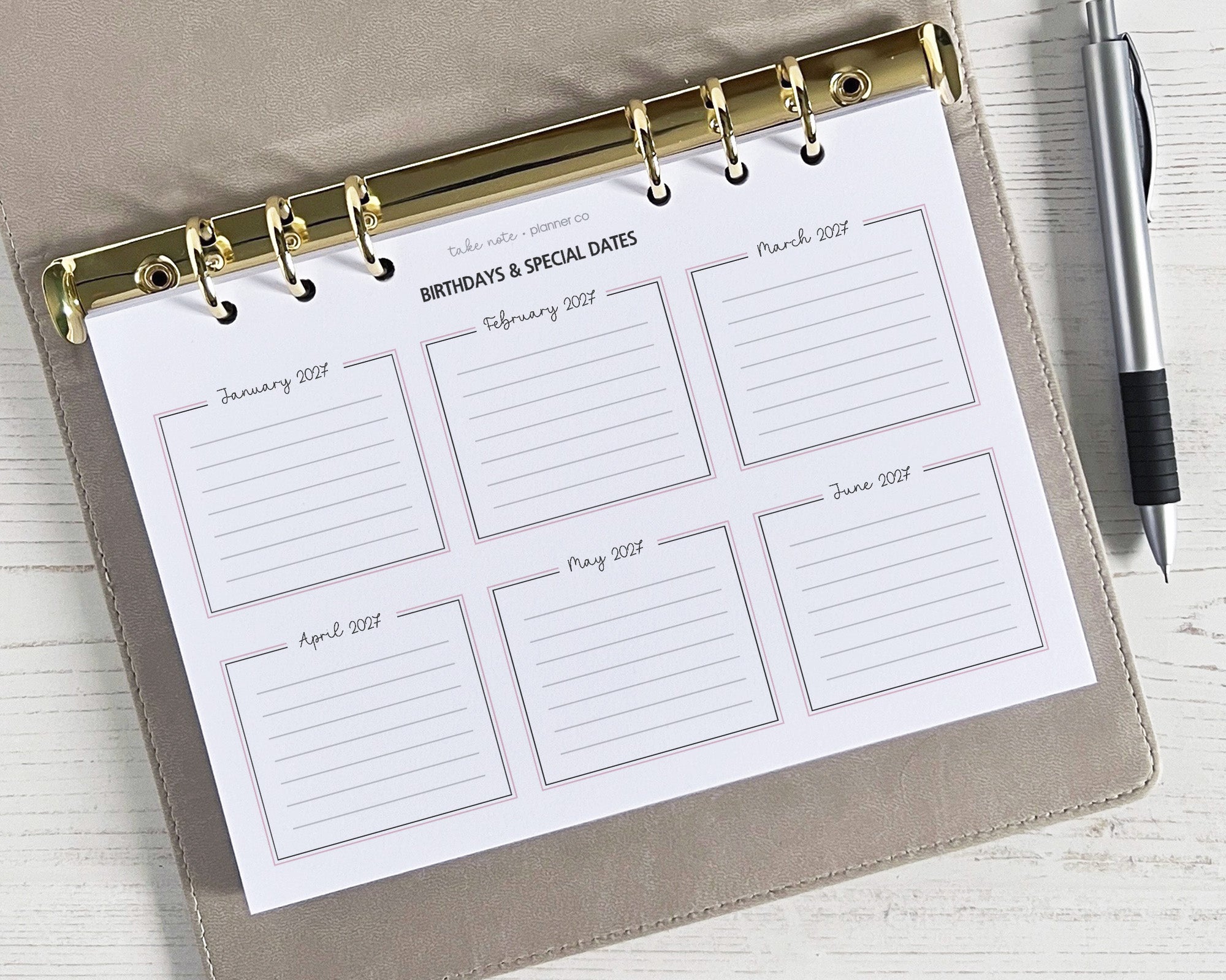 A5 sized yearly overview insert with dates from January to December, designed for use in a planner. The insert is white with golden ring binder tabs and a pen loop, and it's placed on a wooden surface.