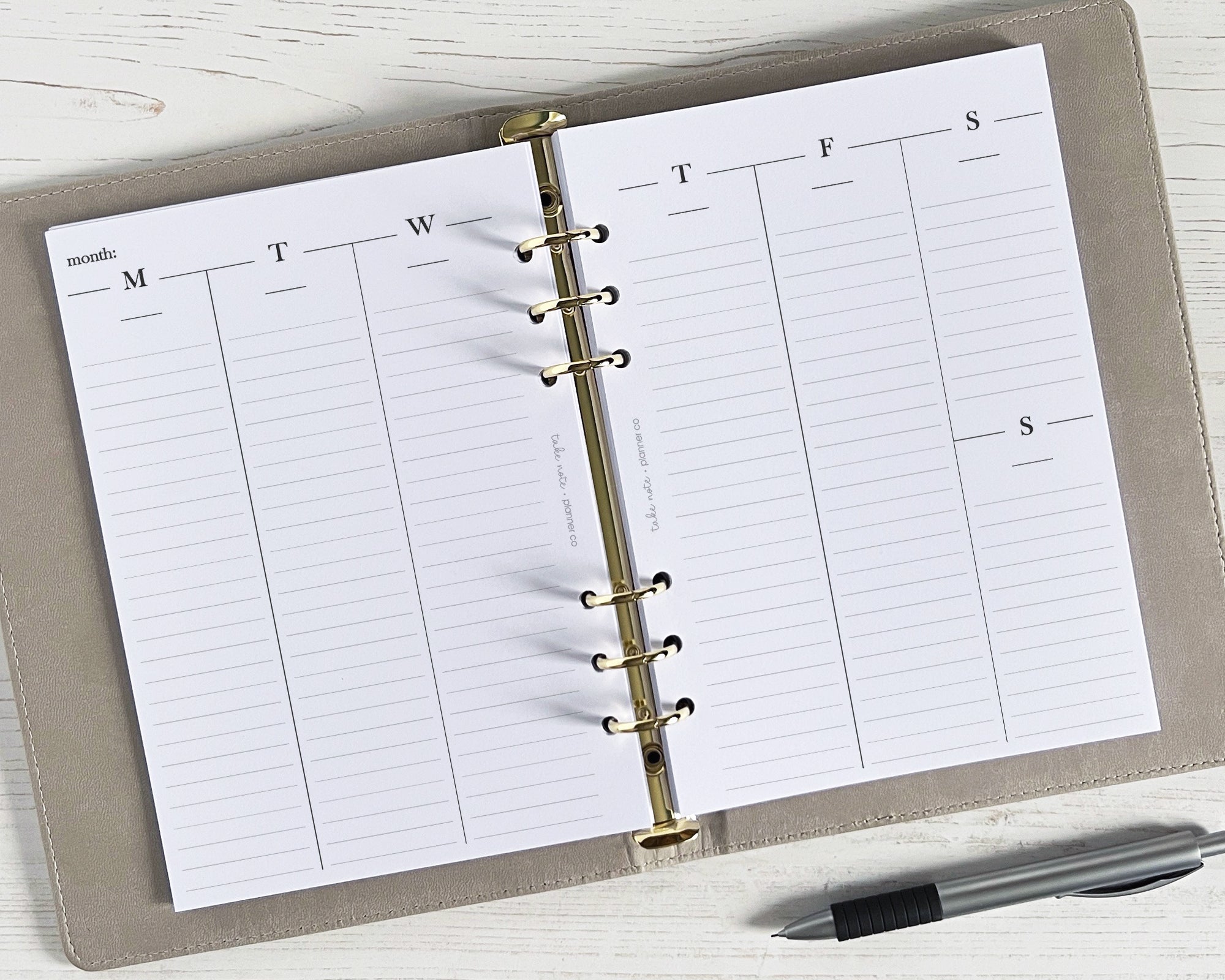 An open weekly planner with undated vertical lines, displayed on a wooden surface with a pen beside it.