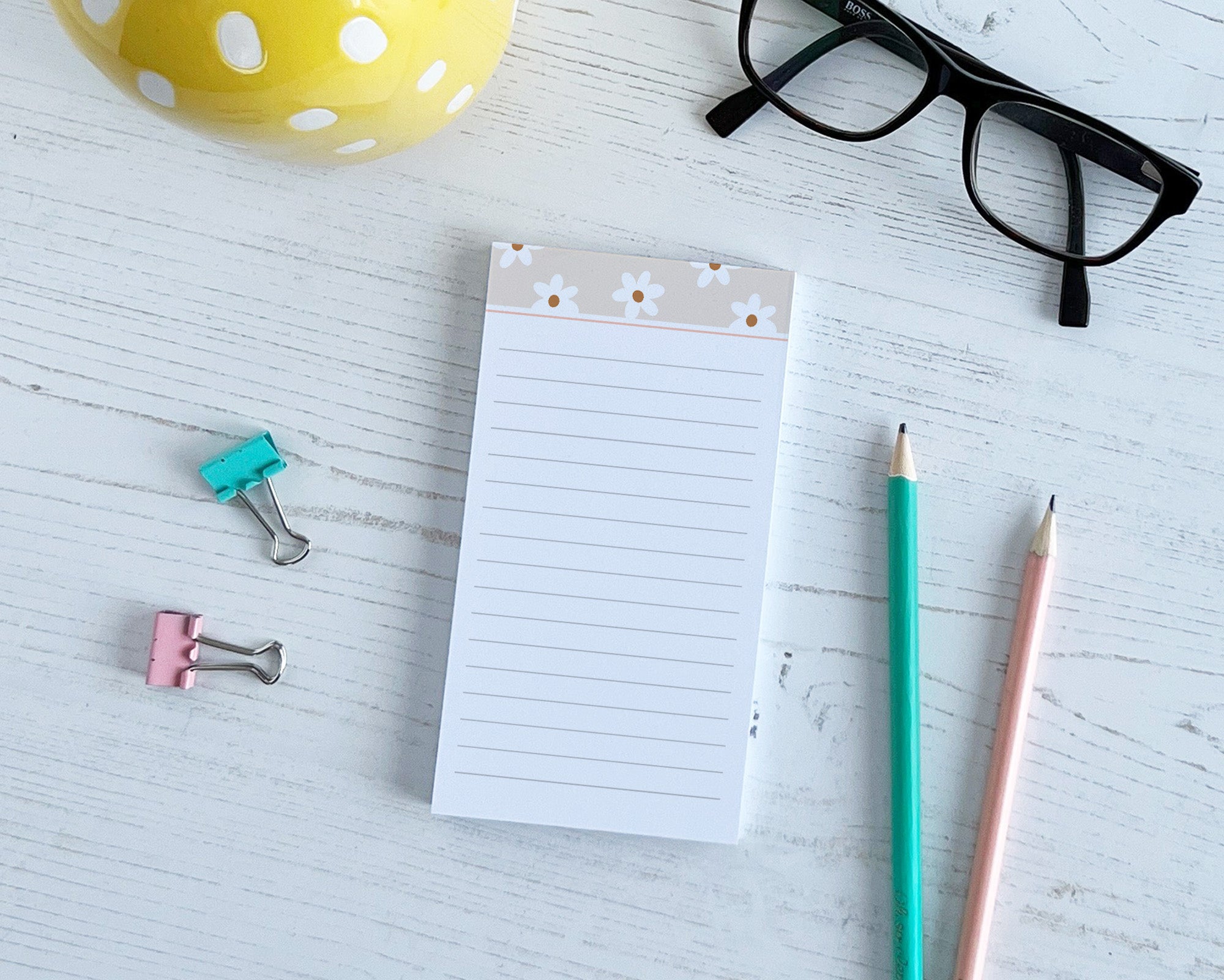 Notepad with pens, clips, and glasses on a light surface