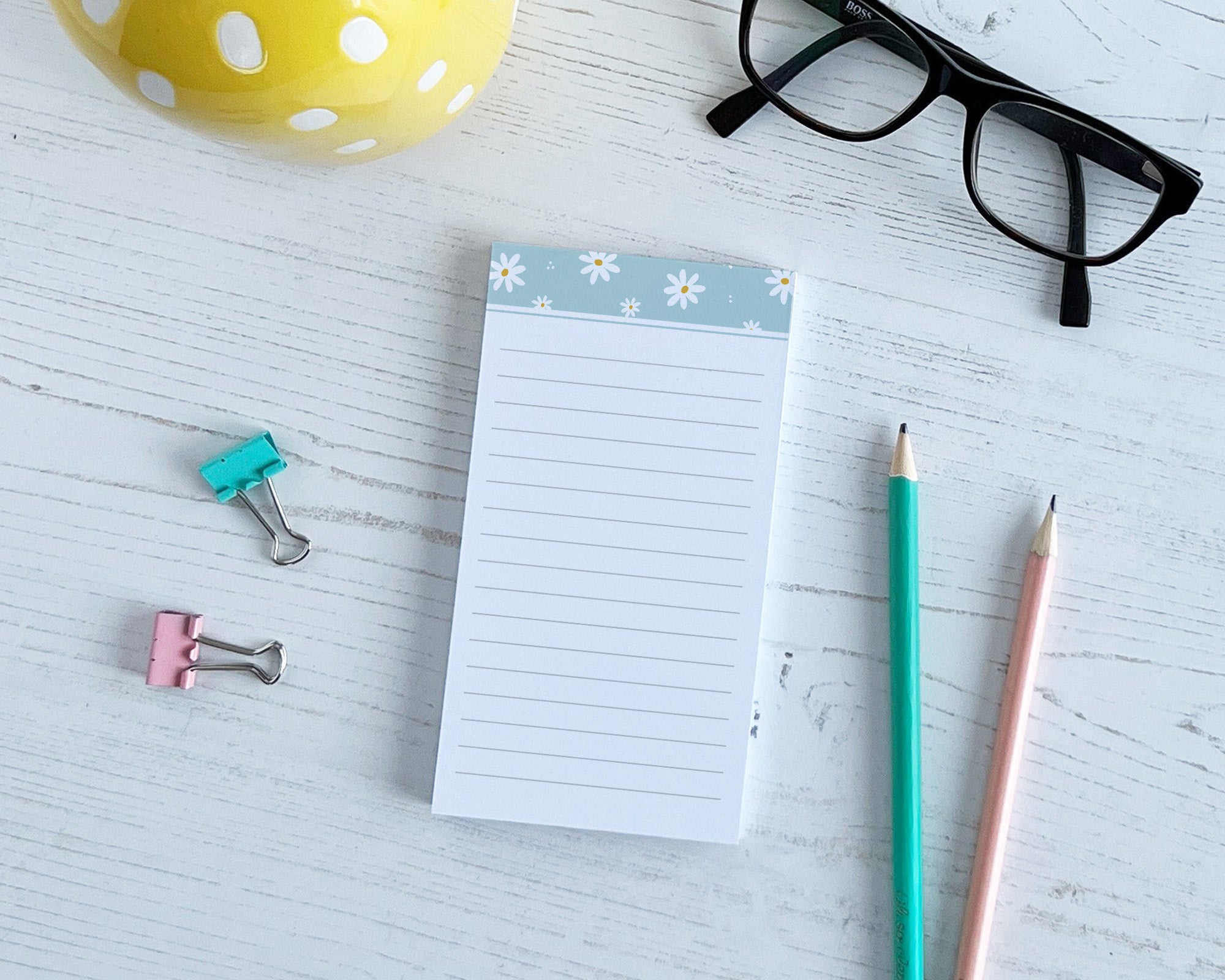 Notepad with floral border, pencils, and stationery items on a light surface