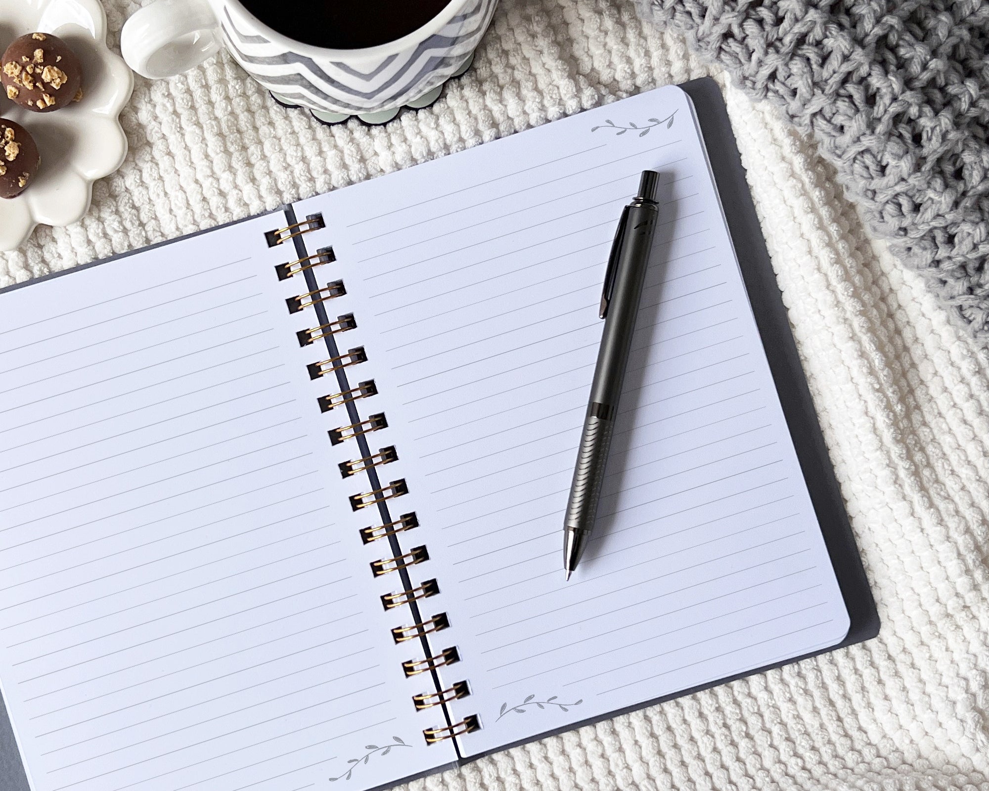 Open journal with a pen on a blanket with a cup and decorative items.