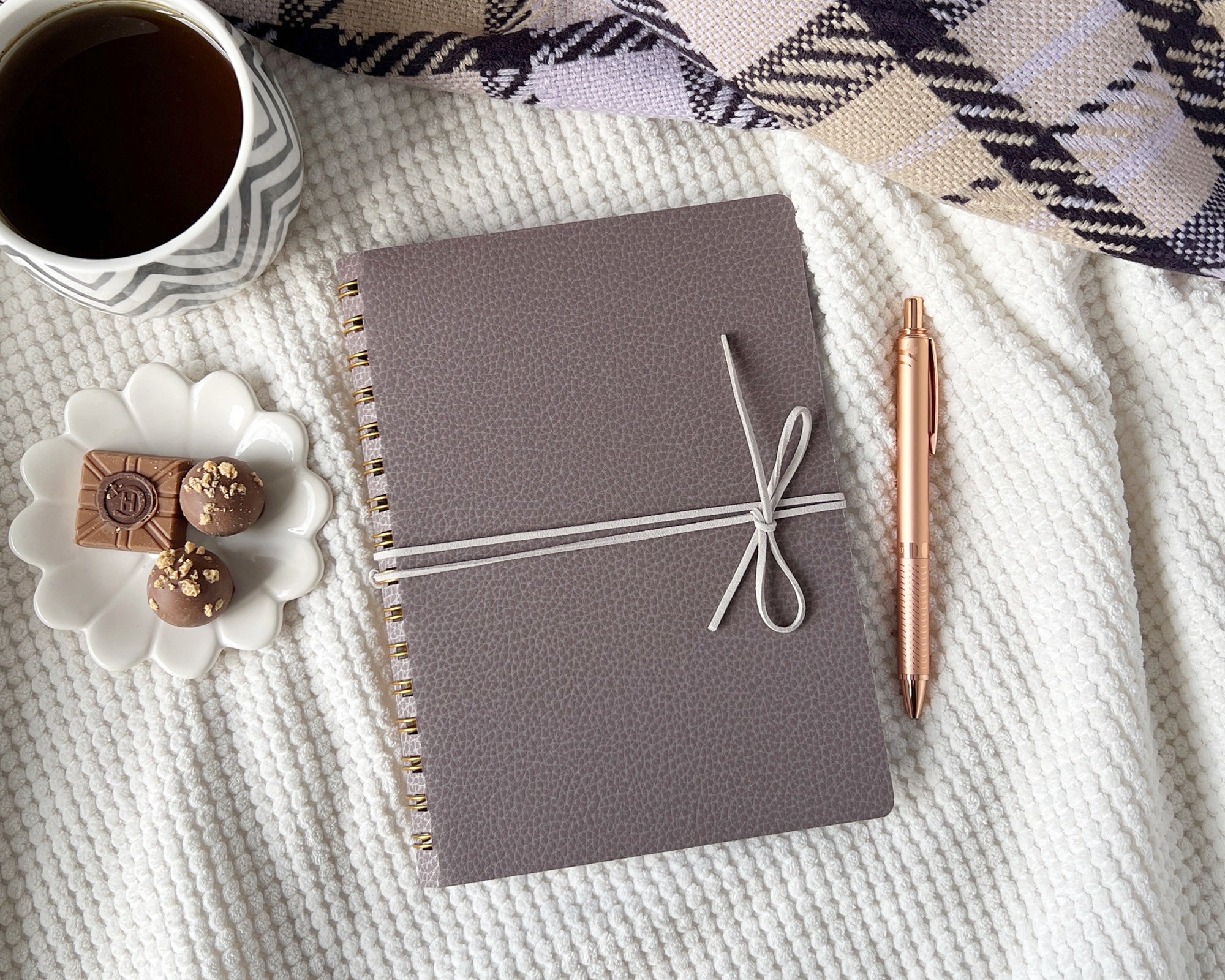 Journal tied with sued cord, next to a cup of coffee and decorative items on a blanket