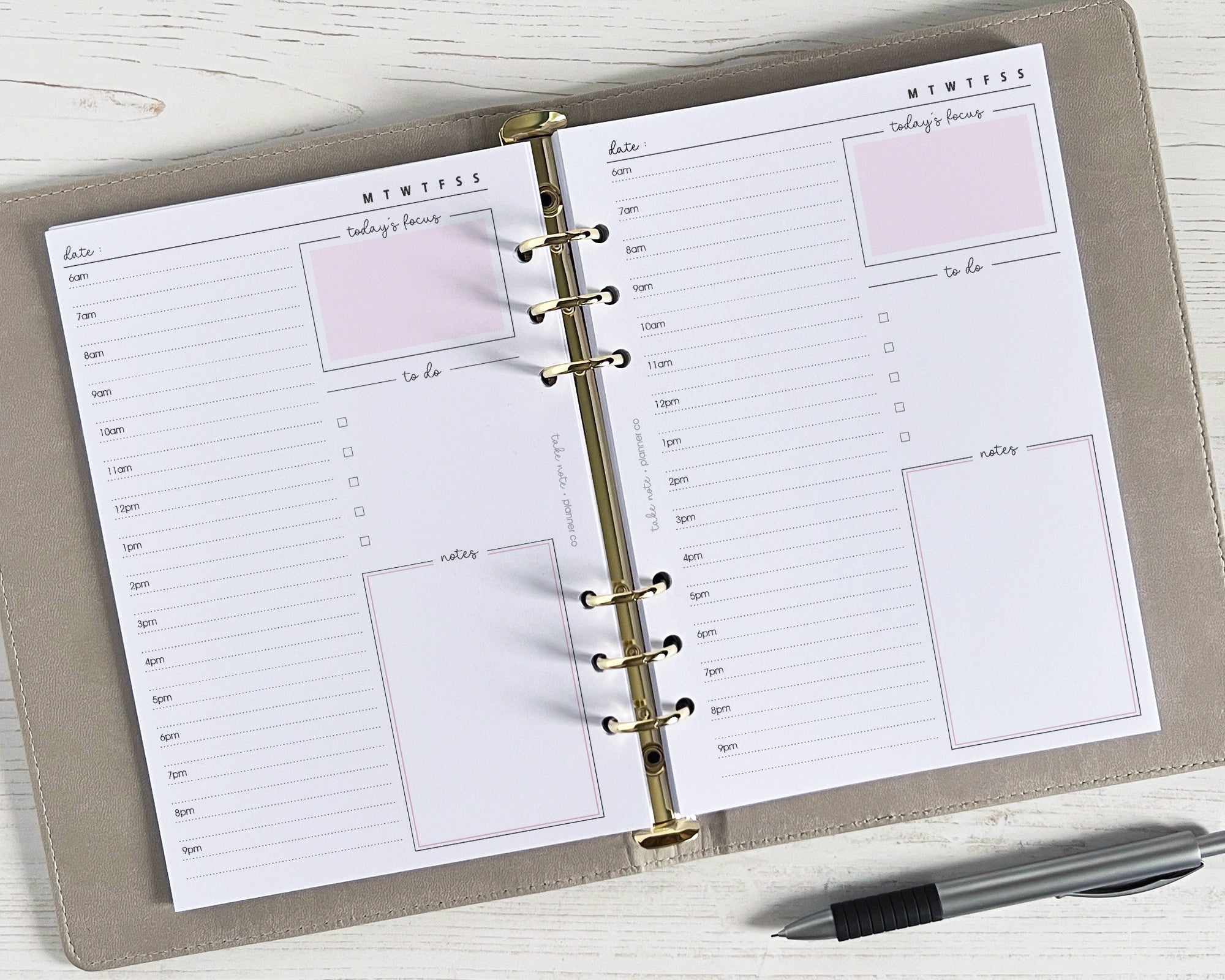 A daily planner insert with half/hourly breakdown, priorities/events box, to do list, and space for notes, displayed on a wooden surface with a pen beside it.