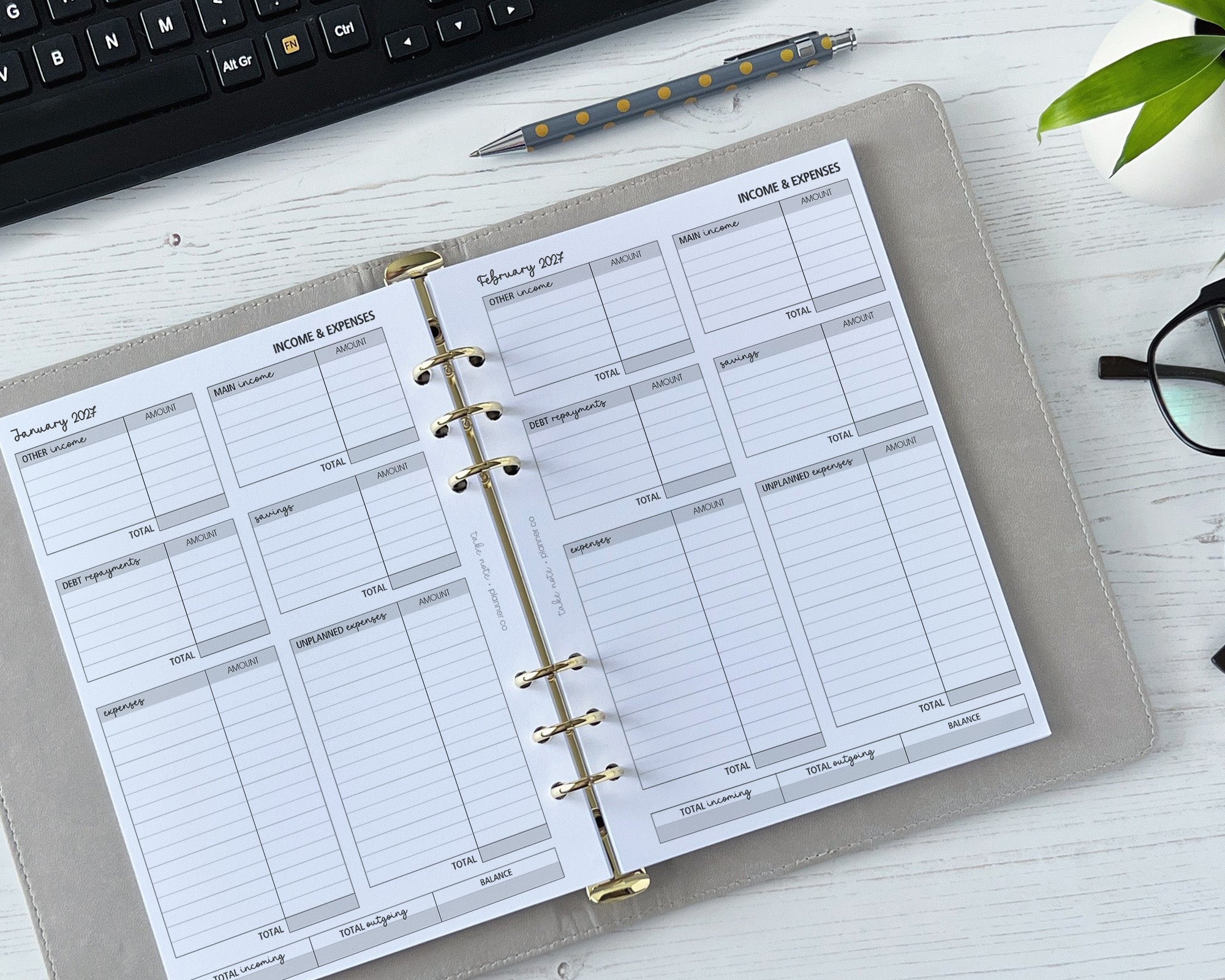 Planner with income and expense tracking pages on a desk with a keyboard and pen.