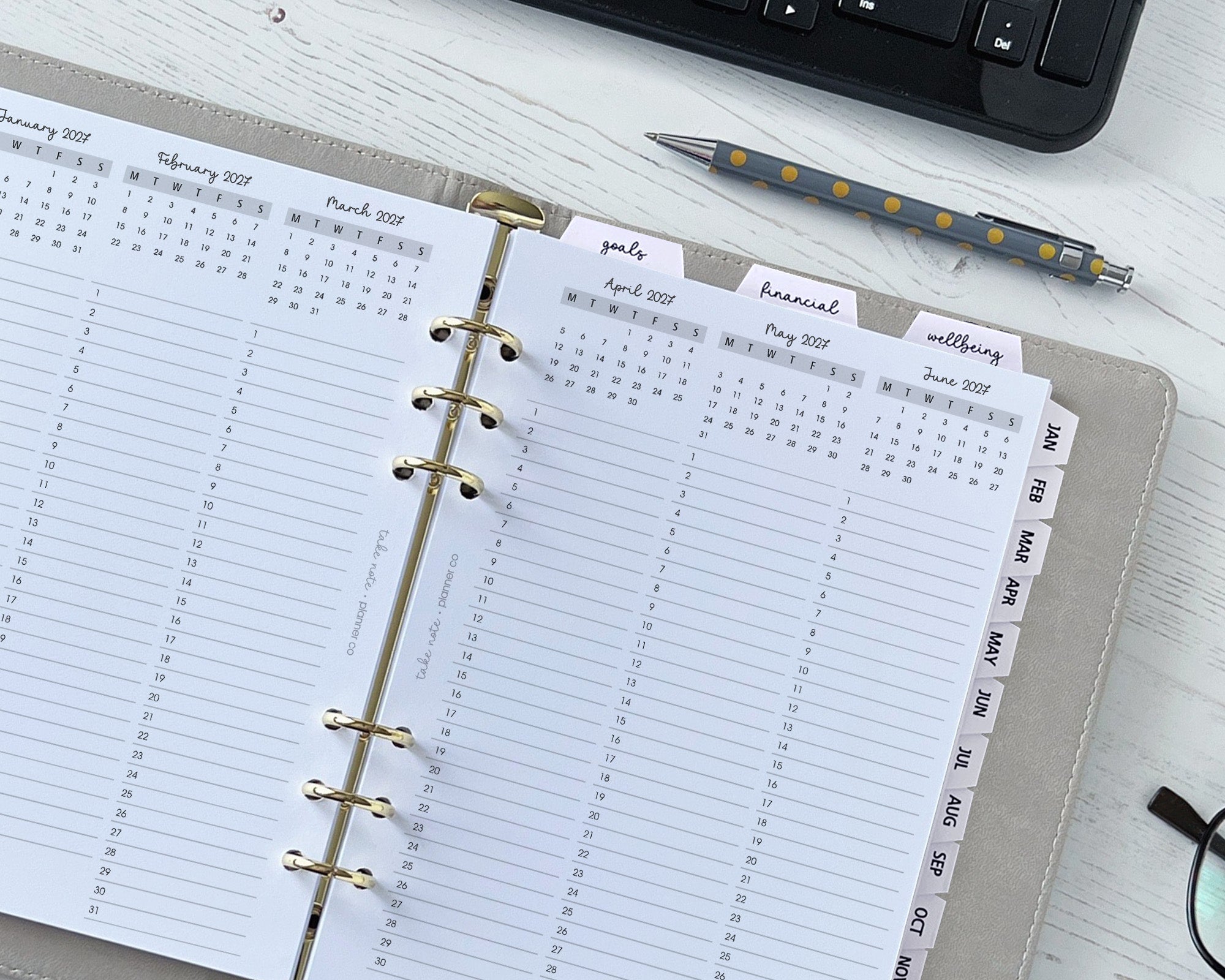 Open planner with calendar pages on a desk next to a keyboard and pen.
