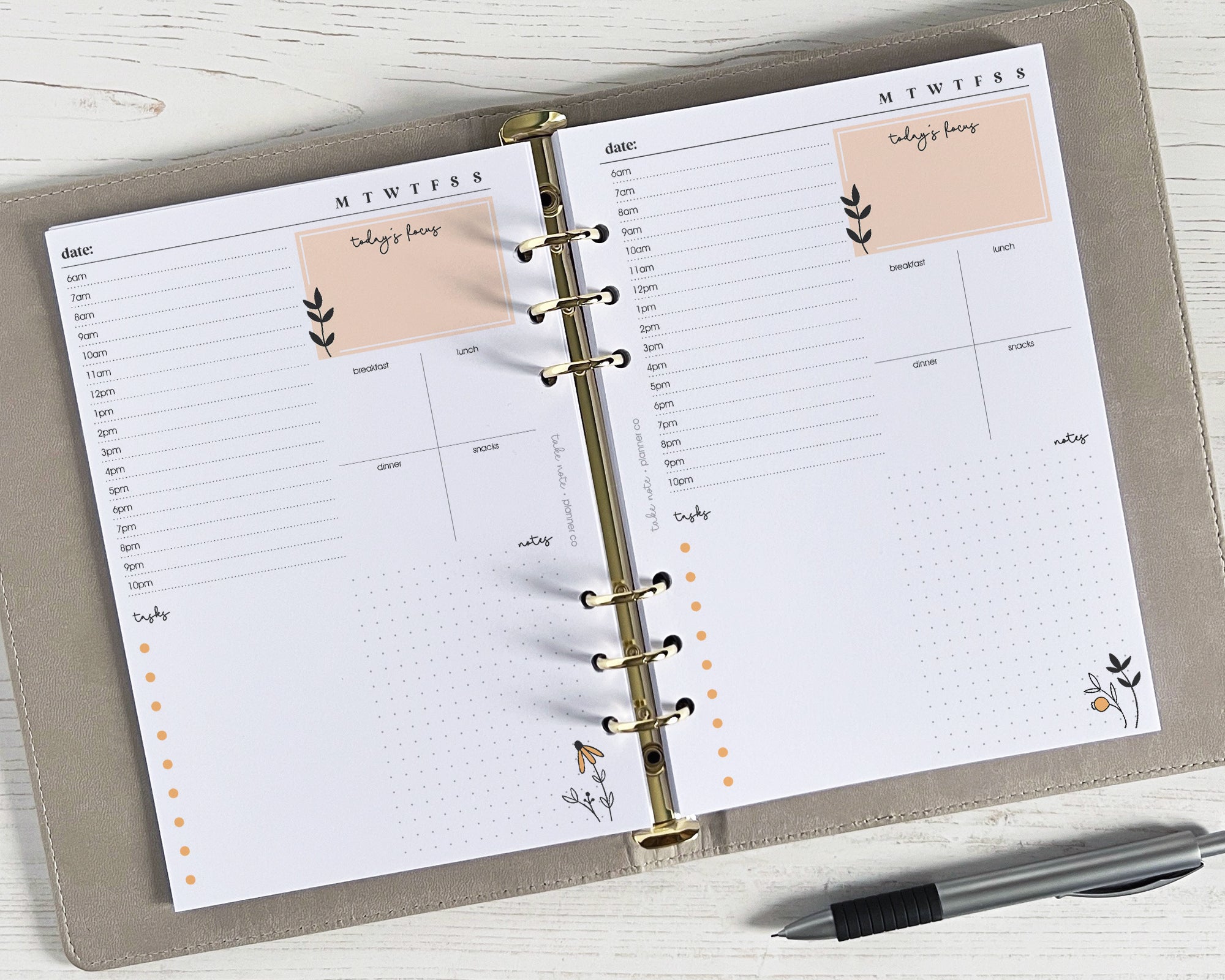 A bright floral undated daily planner insert with a weekly layout with space for notes and a pen beside it on a wooden surface.