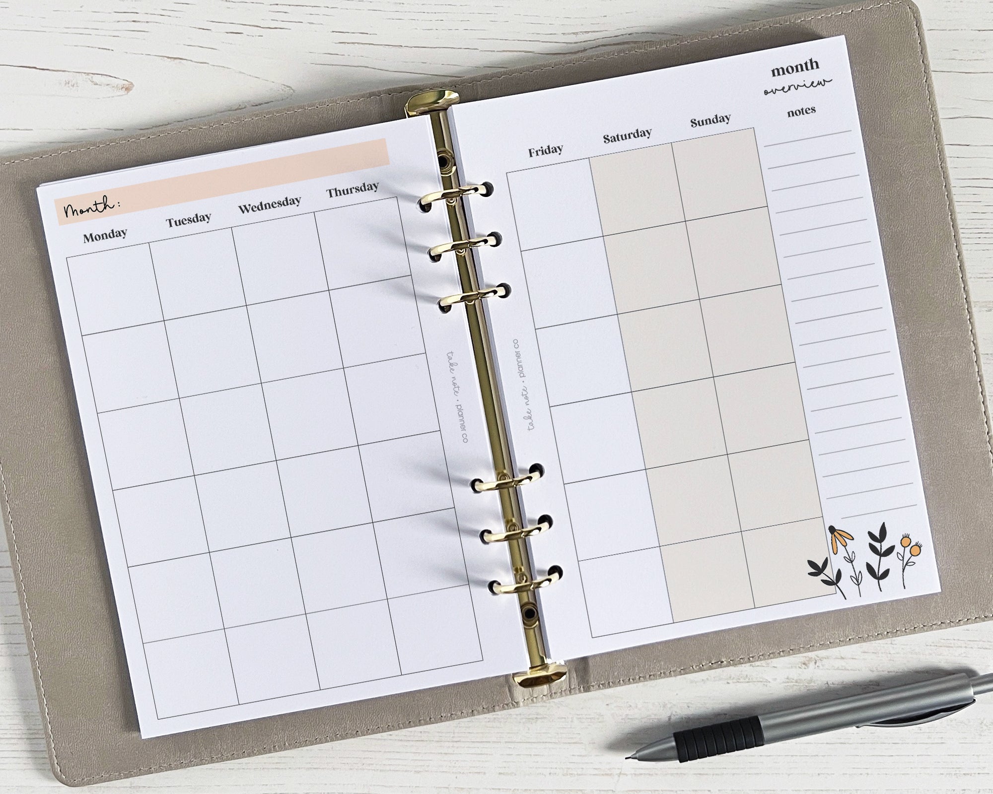 An undated A5 monthly planner insert with a floral design, featuring a two-page spread with weekends, a side panel for additional notes, and gold-colored grommets.