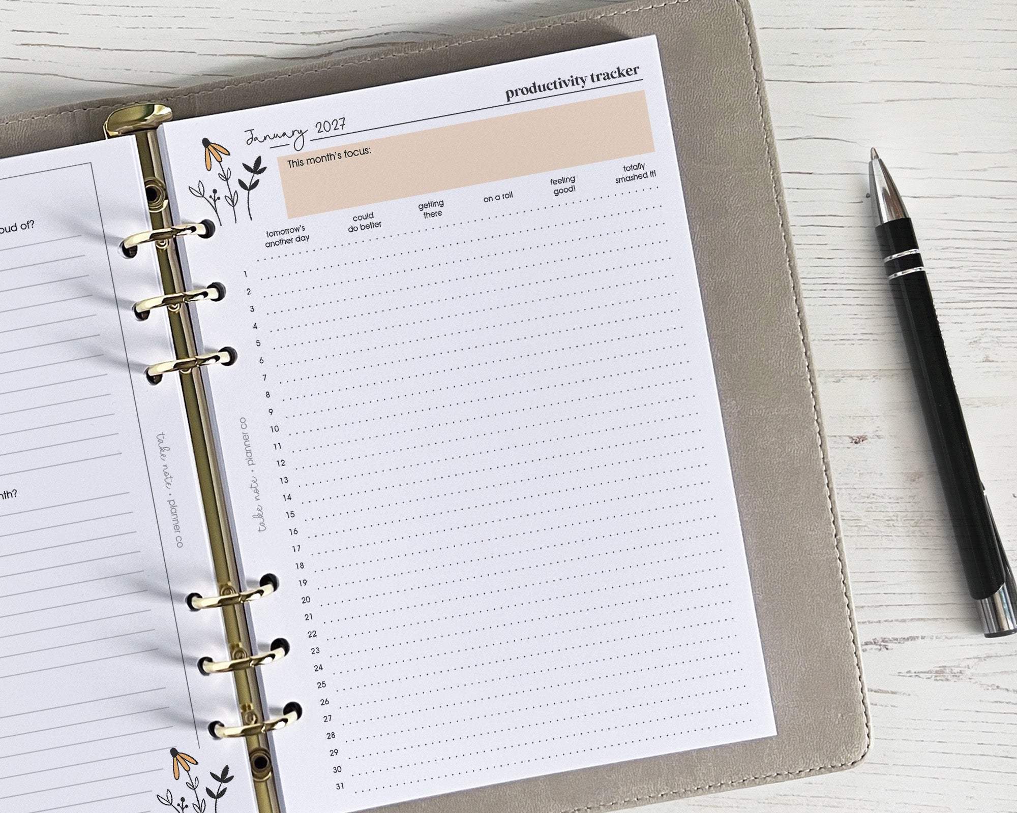 Open planner with productivity tracker page on a white surface next to a pen
