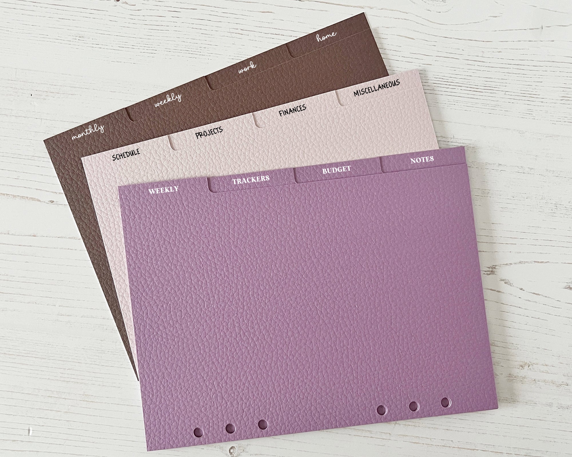 Three planner dividers with different colour schemes and fonts on a white surface