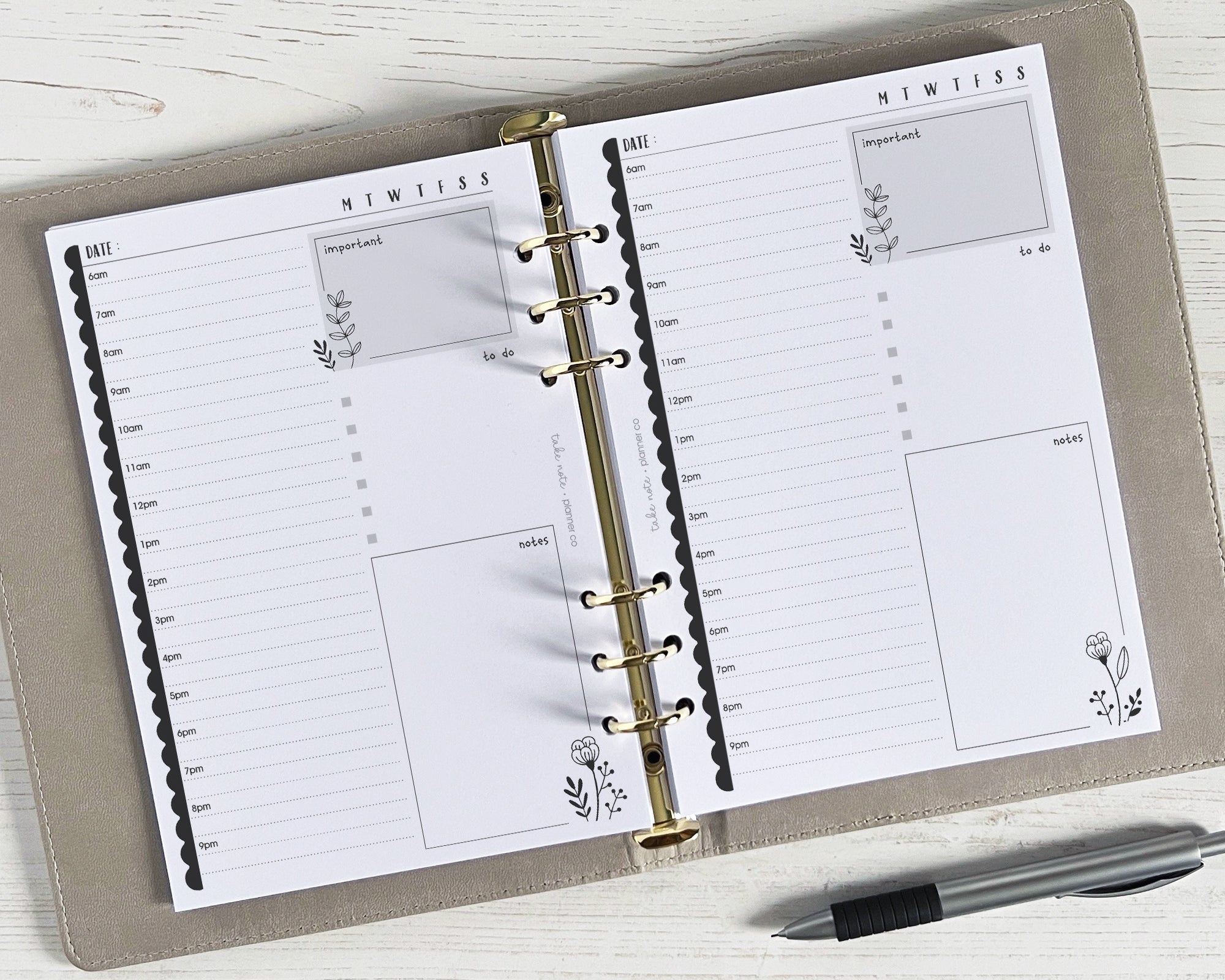 A photo of daily planner inserts with a monochrome floral design, featuring a day's schedule with sections for notes, events, and to-do list, displayed on a wooden surface with a pen alongside.