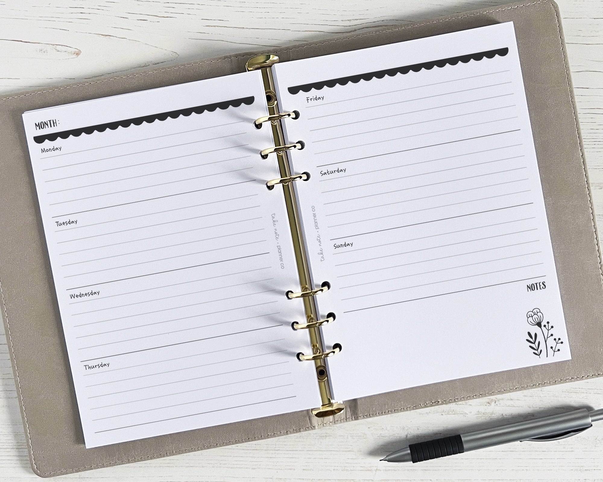 A5 weekly planner inserts with a monochrome floral design, undated, displayed open on a table with a pen alongside.