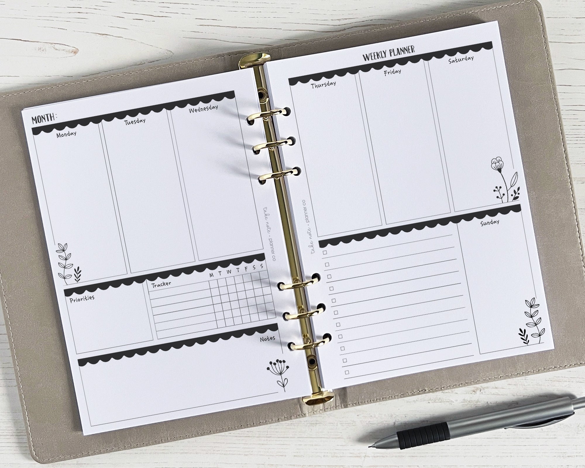 A5 weekly planner inserts with a monochrome floral design, undated, displayed open in a ring binder with a pen lying beside it.