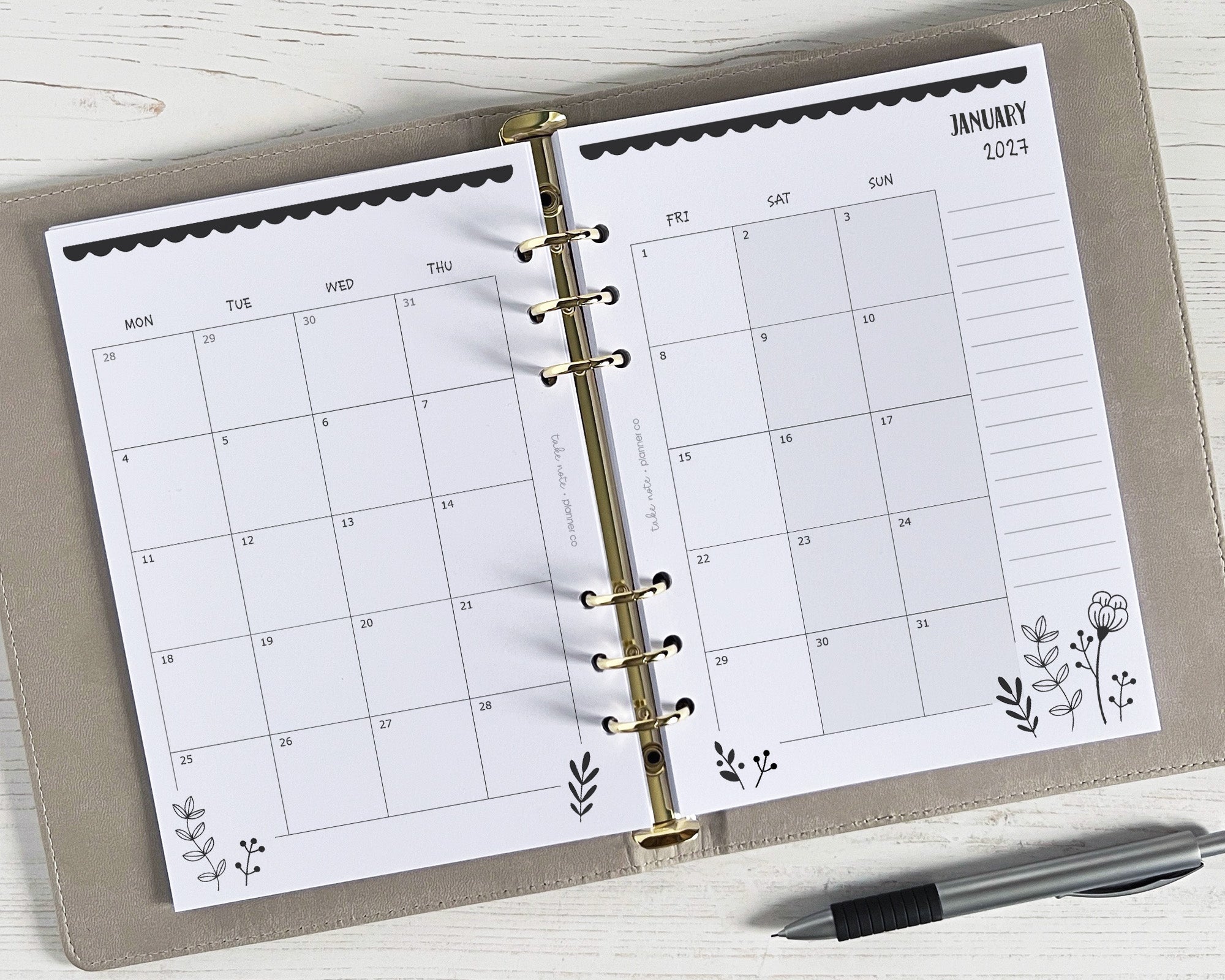 A5 monthly planner inserts with a monochrome floral design, displayed in a binder with a pen for scale.