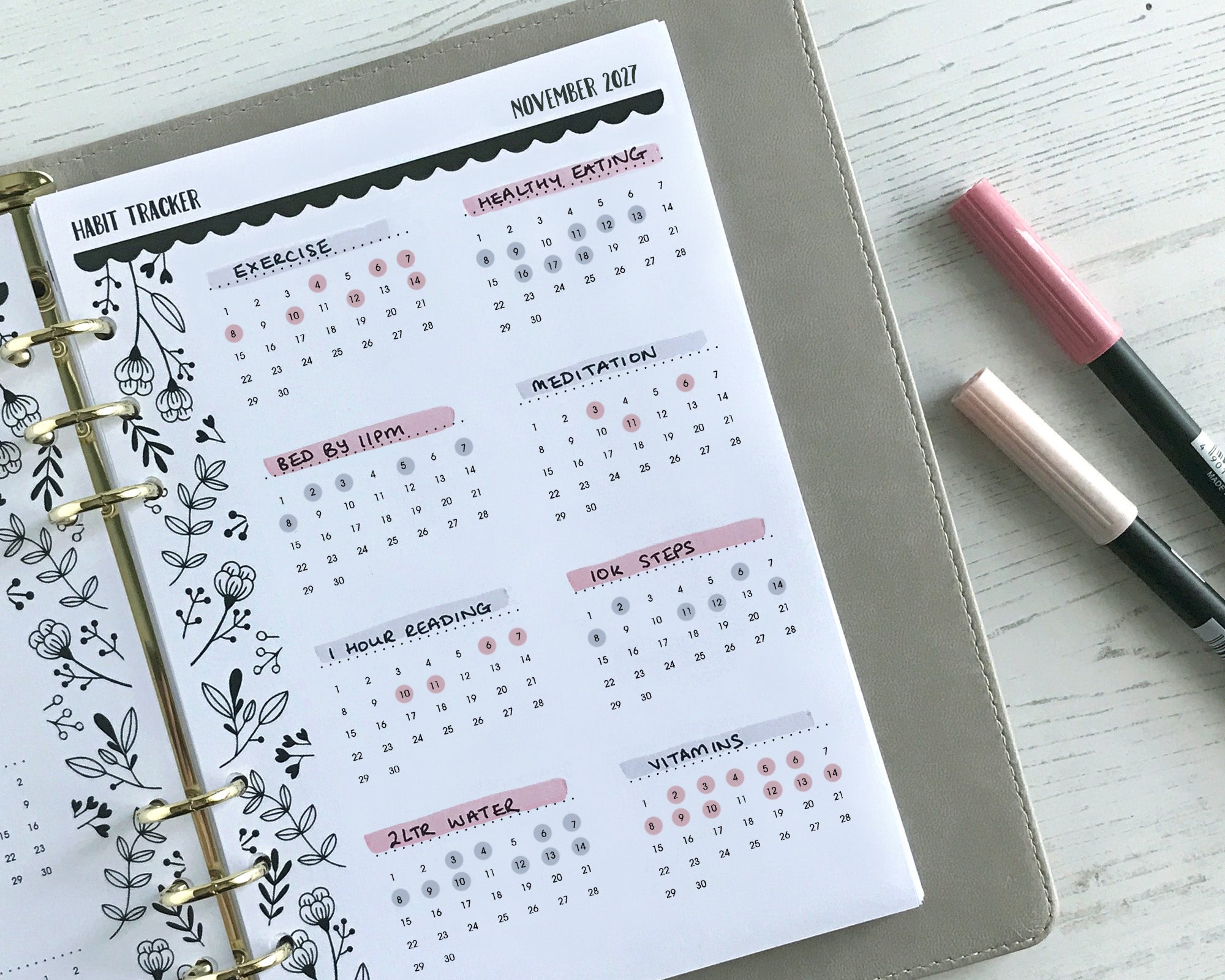 A monthly habit tracker insert with a monochrome floral design, displayed in an open planner with pens alongside.