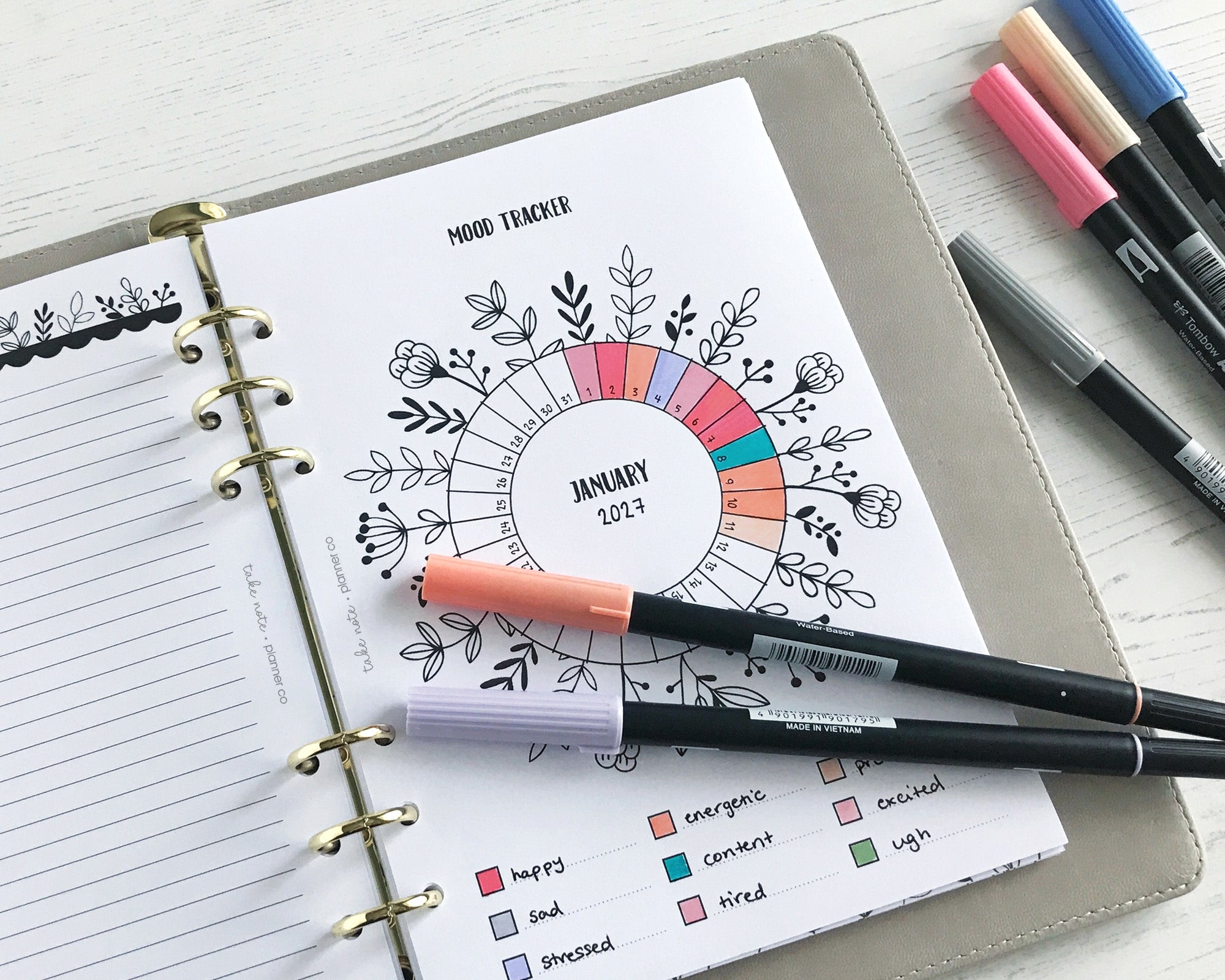 Planner with a mood tracker inserts and coloured markers on a white surface