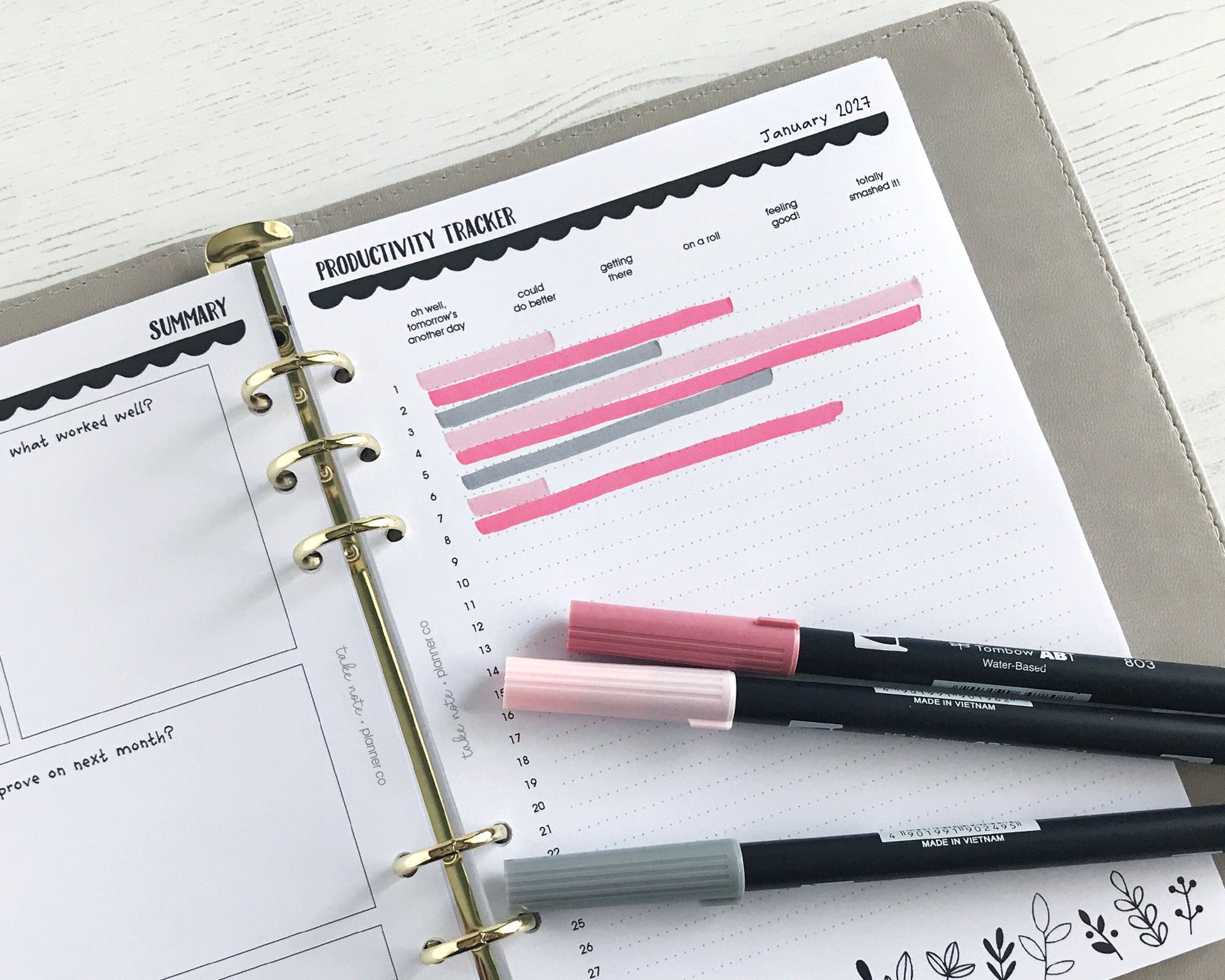 Productivity tracker with floral design and two pens on a white surface