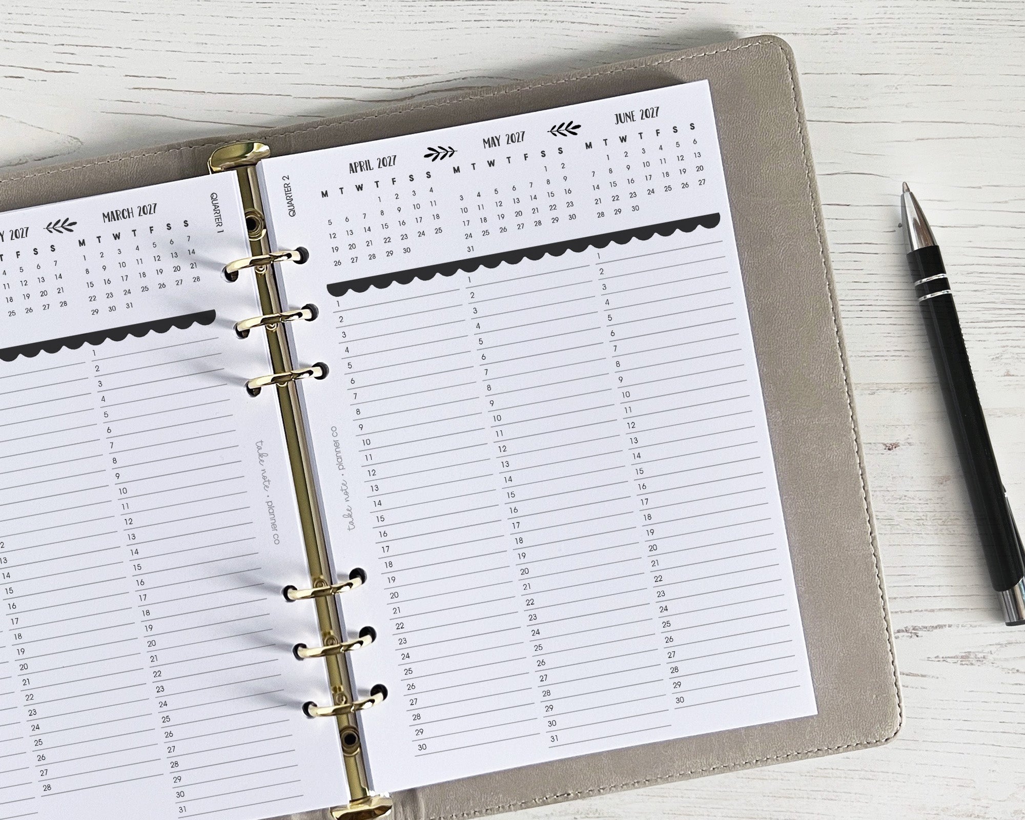 A planner with quarterly overview inserts and a pen on a wooden surface.