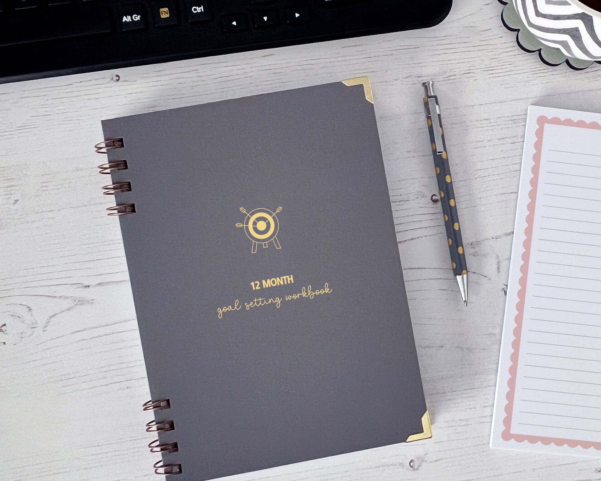 goal setting workbook with a target and arrows icon on the cover on a white surface with a keyboard and pen.