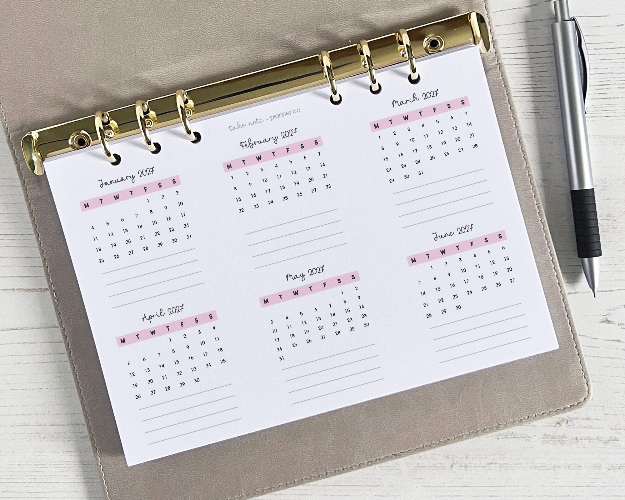 A5 sized yearly overview insert with a double-sided design, featuring a monthly calendar layout with space for notes, placed inside a planner with a pen beside it.