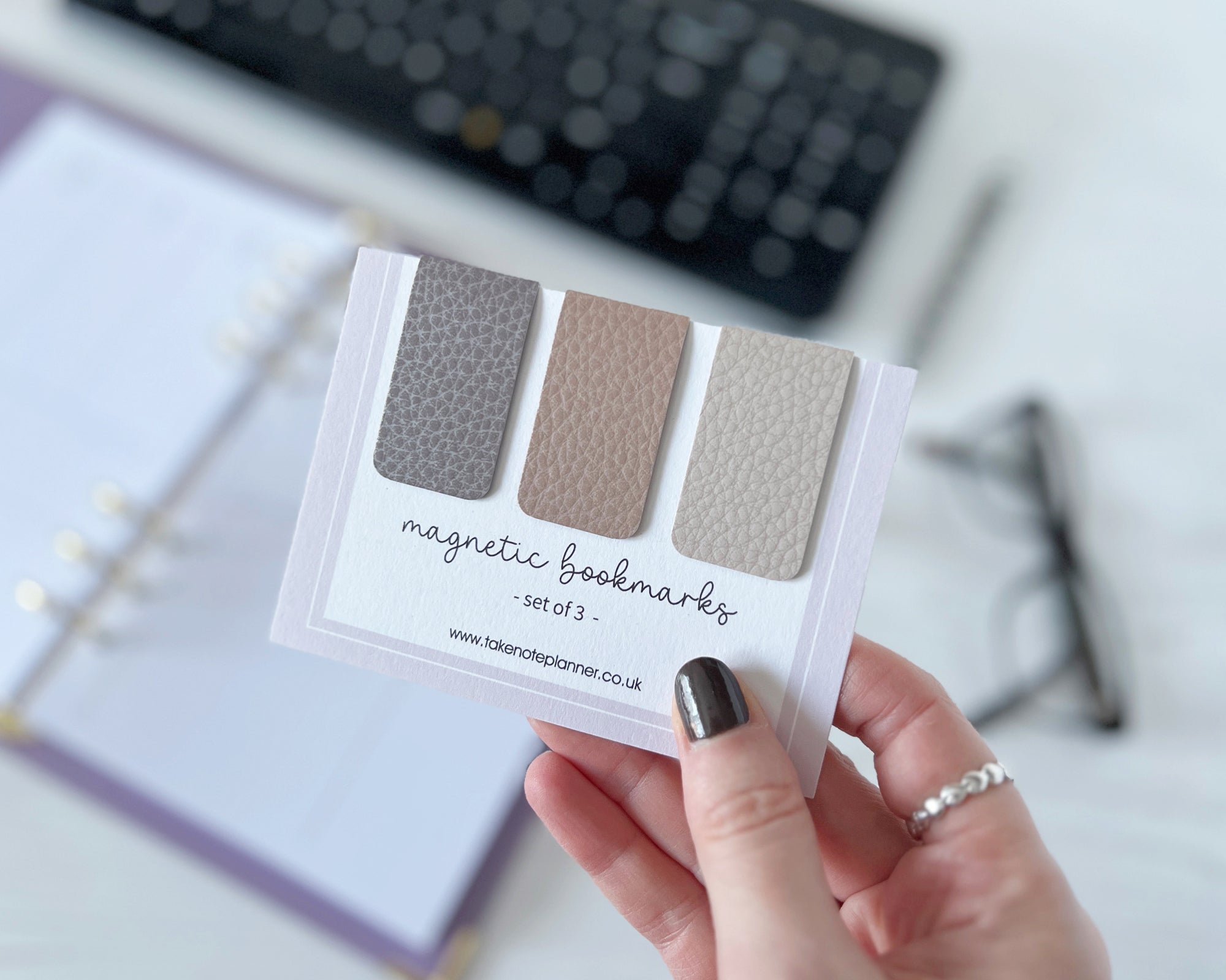 Hand holding a set of magnetic bookmarks with three color swatches, blurred office background