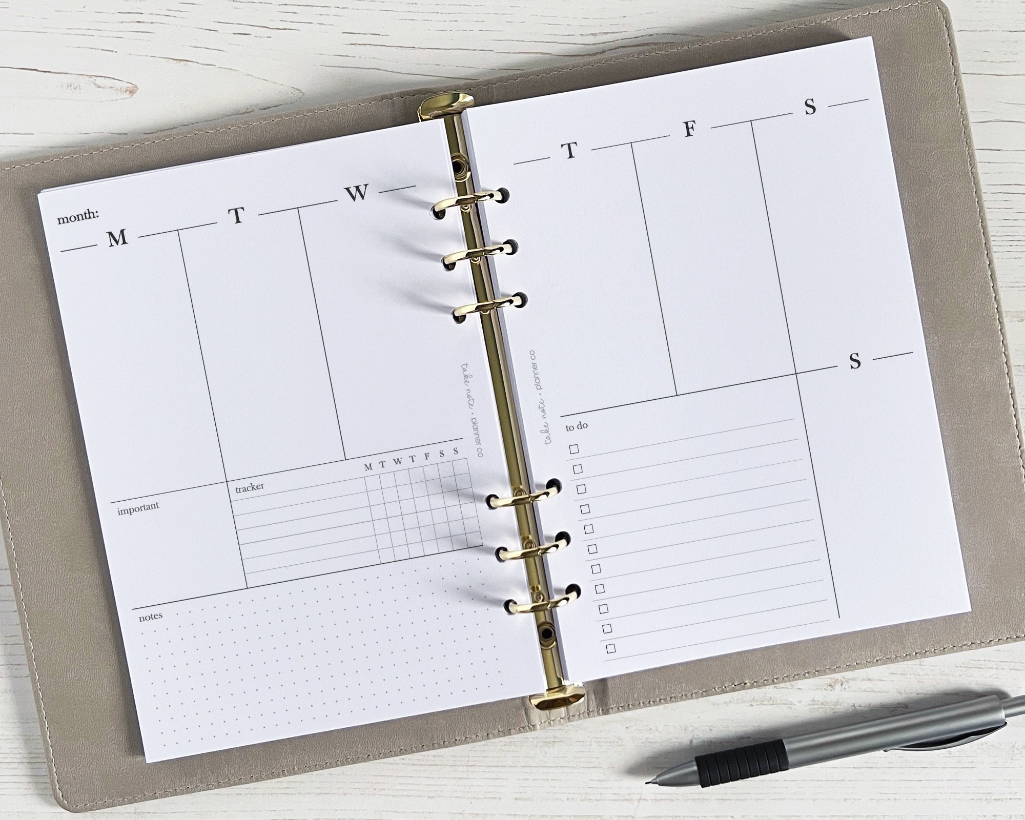An open weekly planner insert with a minimalist design, showing spaces for daily schedules and appointments, with a pen beside it.