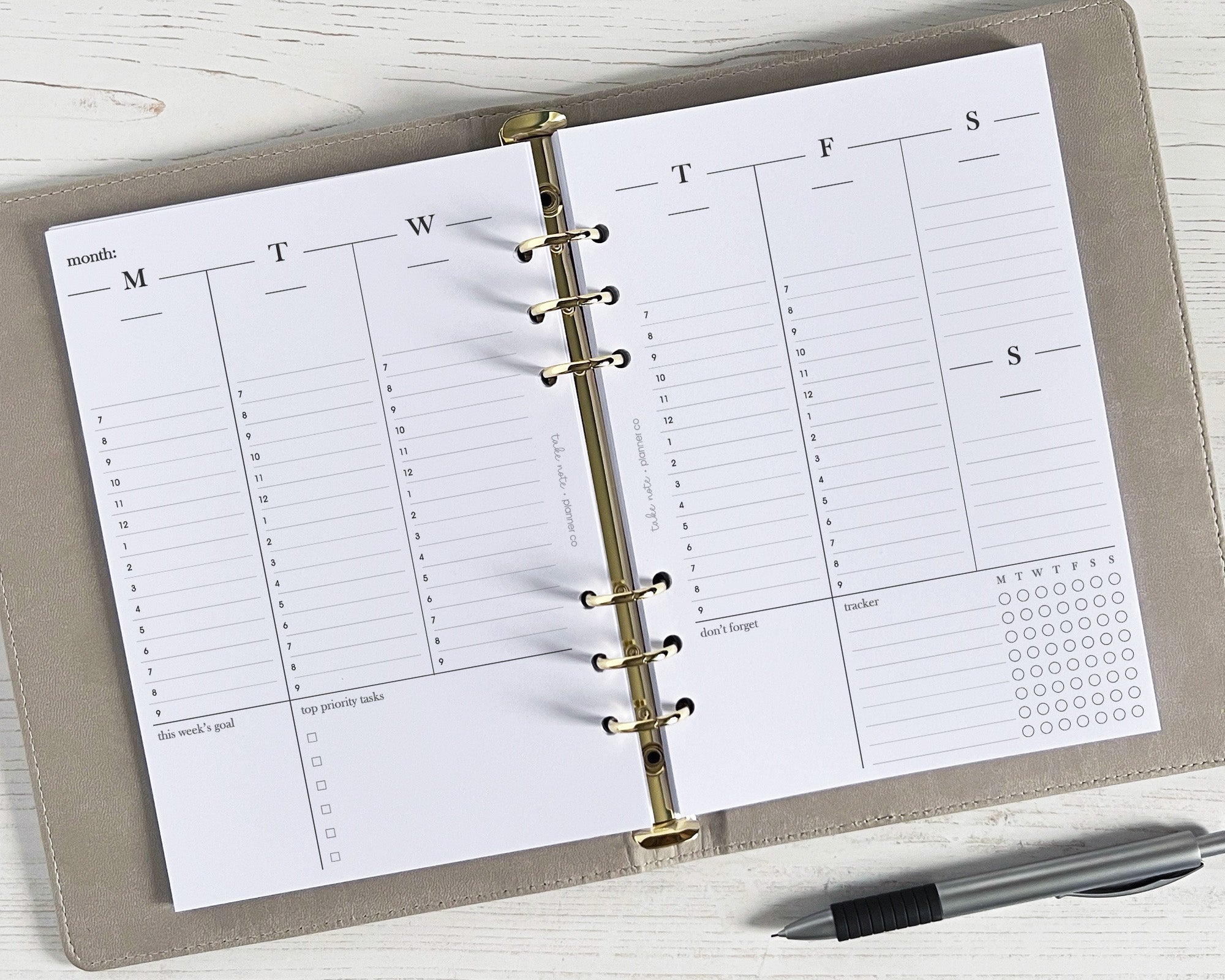 Open planner with calendar pages on a white surface, pen to the side