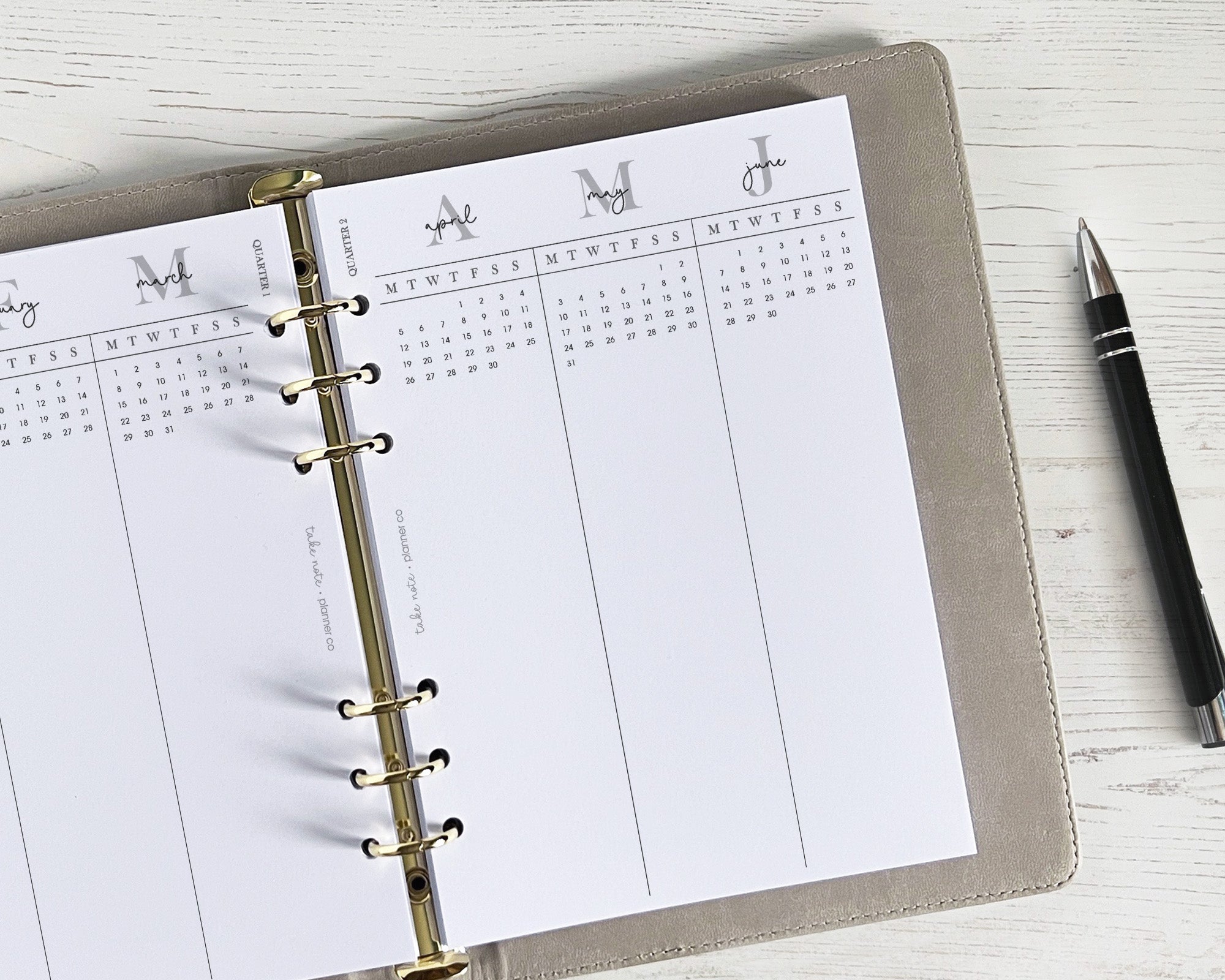 A planner with quarterly overview inserts and a pen on a wooden surface.