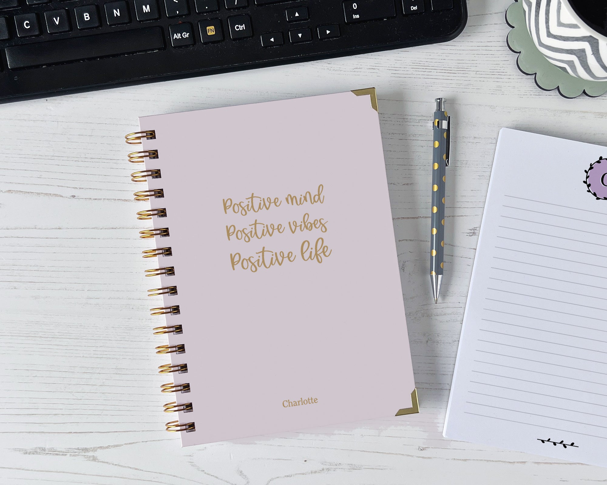 Pink notebook with motivational quote on a desk with a keyboard and pen.