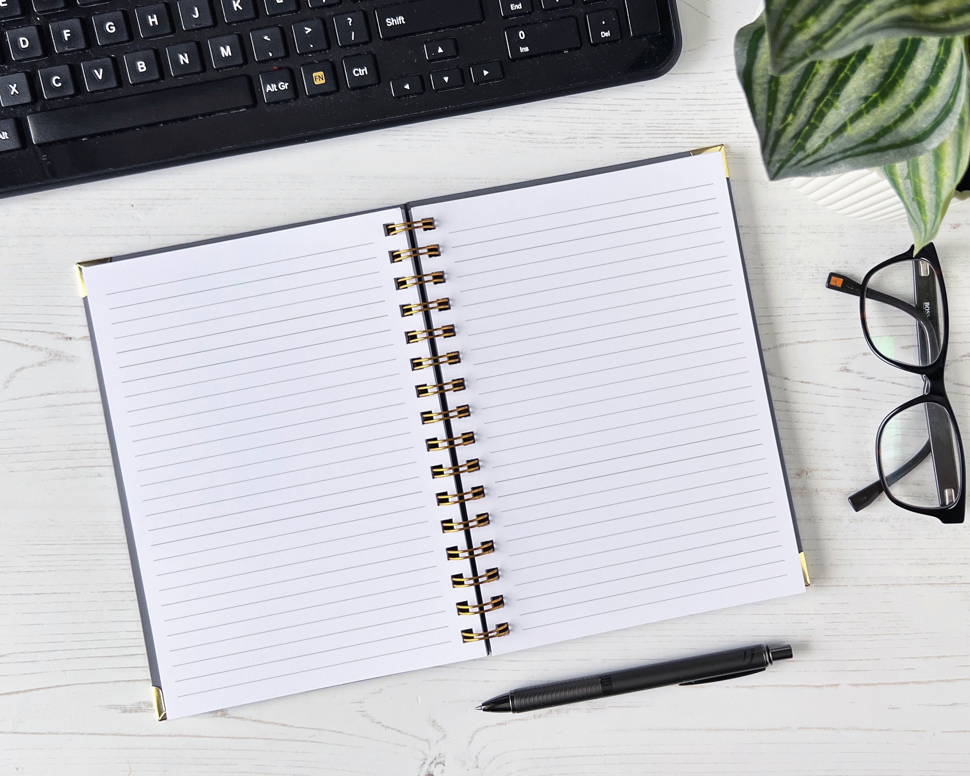 Open notebook with lined pages on a desk with a keyboard, glasses, and pen.