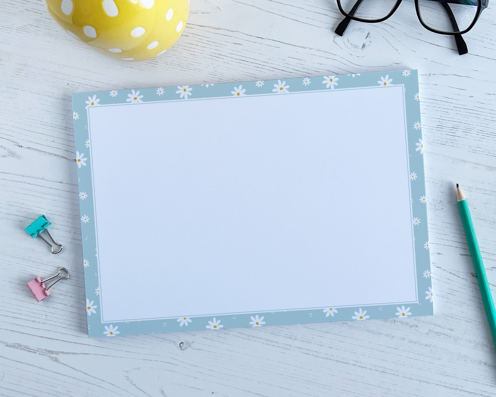 Deskpad with floral border on a light wooden surface with stationery items.